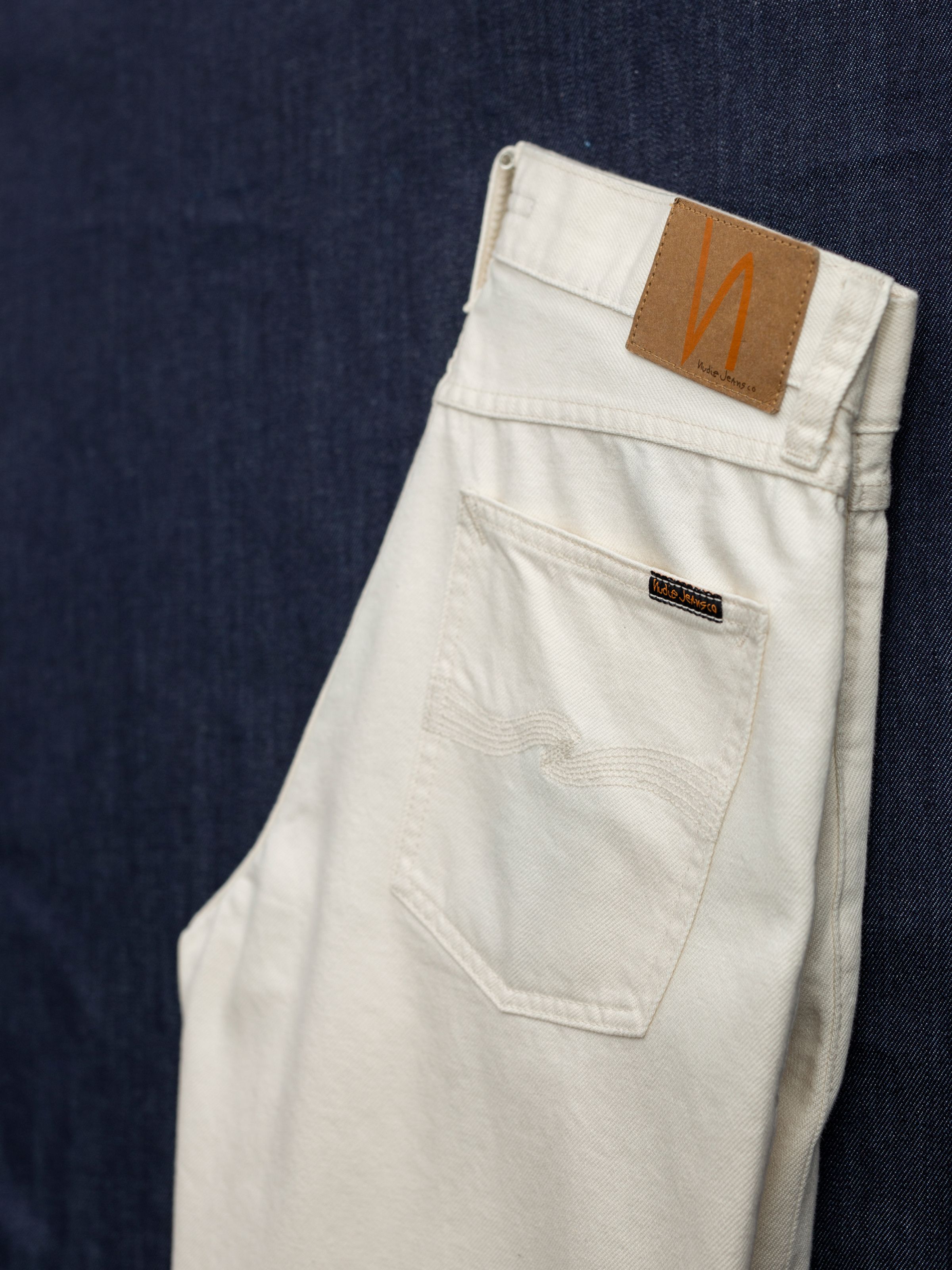 Nudie Jeans Rad Rufus Everivory, close-up of the back pocket and brown Jacron patch on ivory rigid denim jeans.