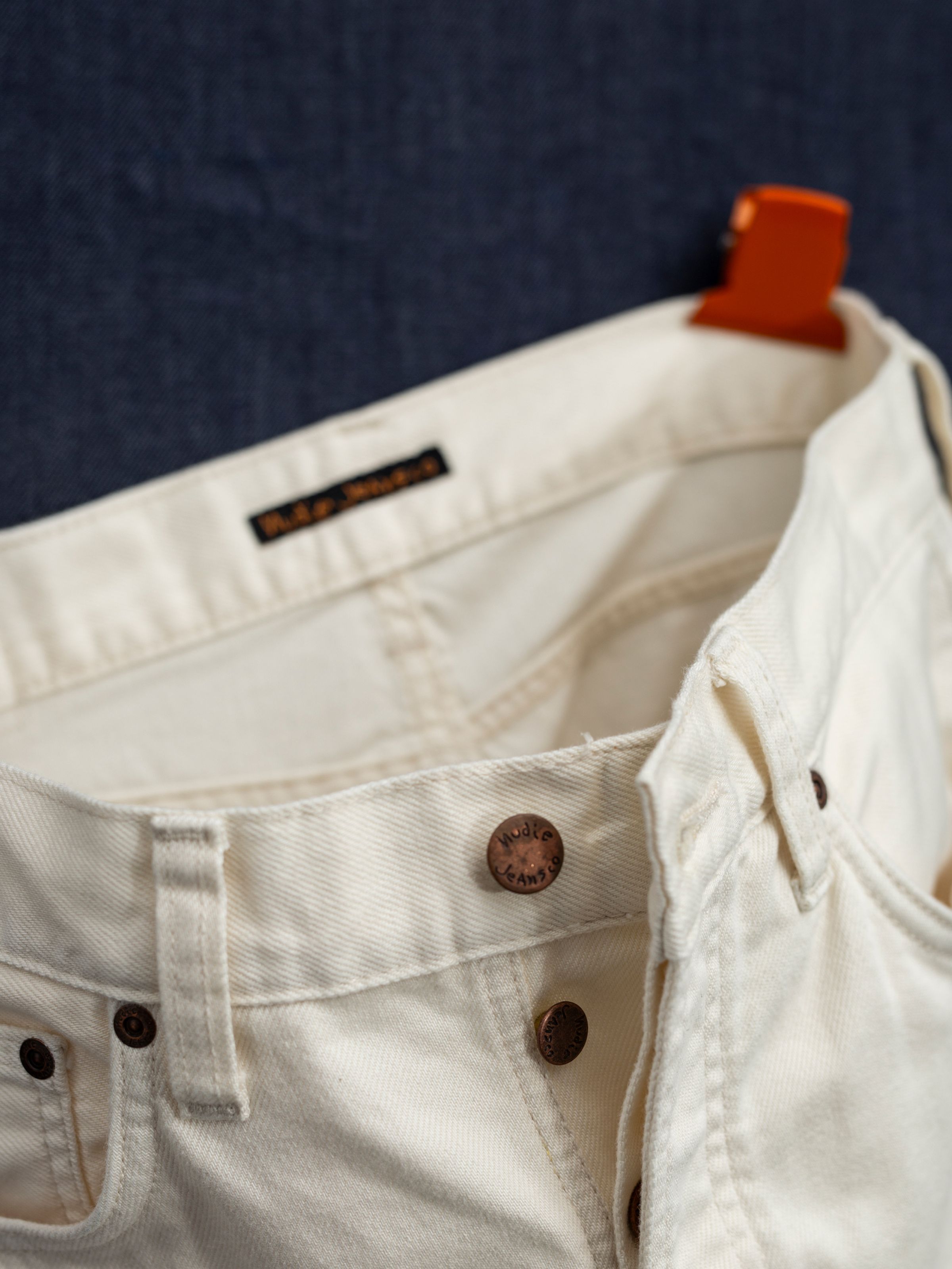 Nudie Jeans Seth Shorts Everivory, close-up of the rigid ivory denim waistband showing the copper button fly.
