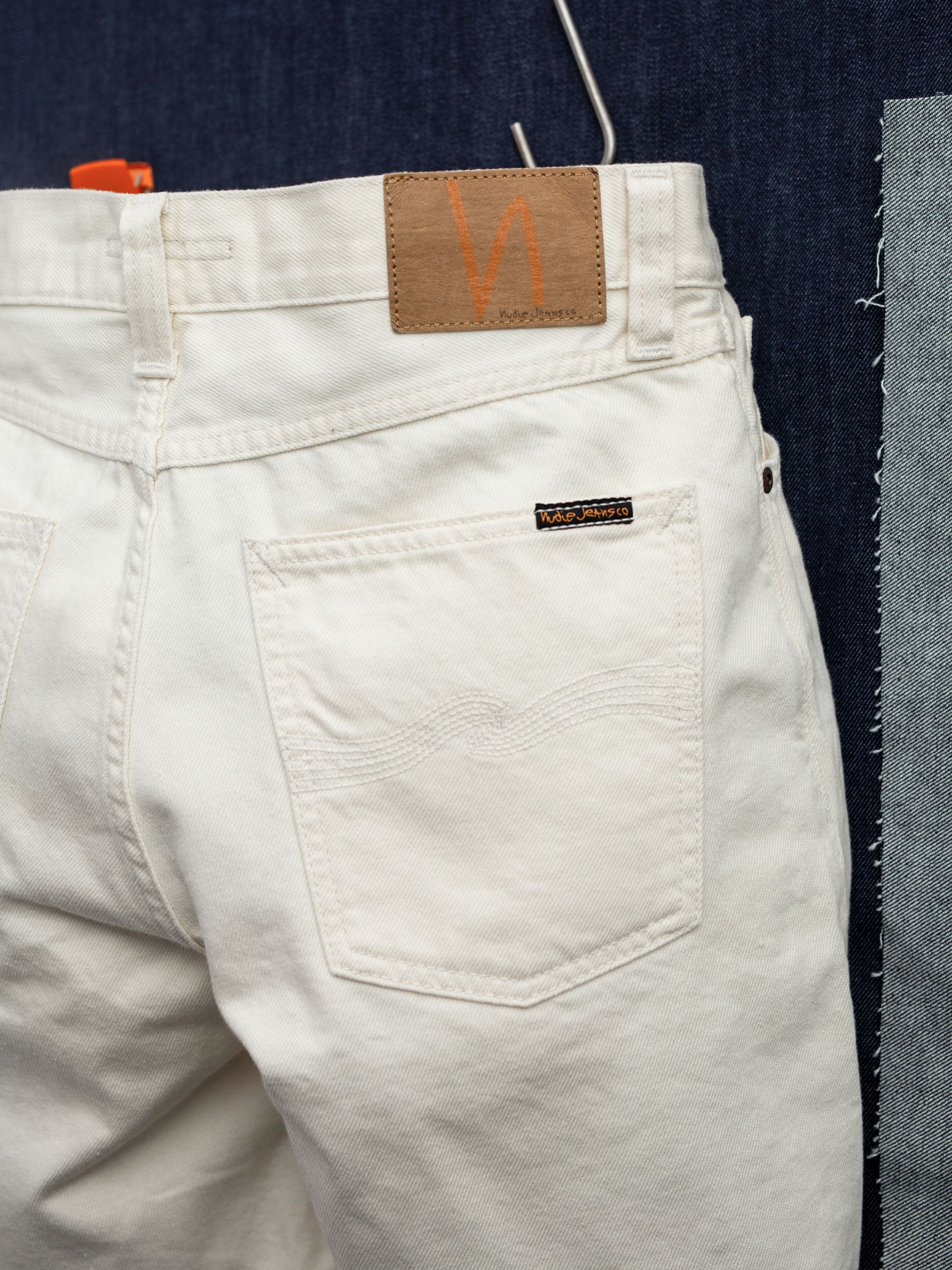 Nudie Jeans Seth Shorts Everivory, close-up of the back pocket wavy embroidery and logo patch on rigid ivory cotton denim.