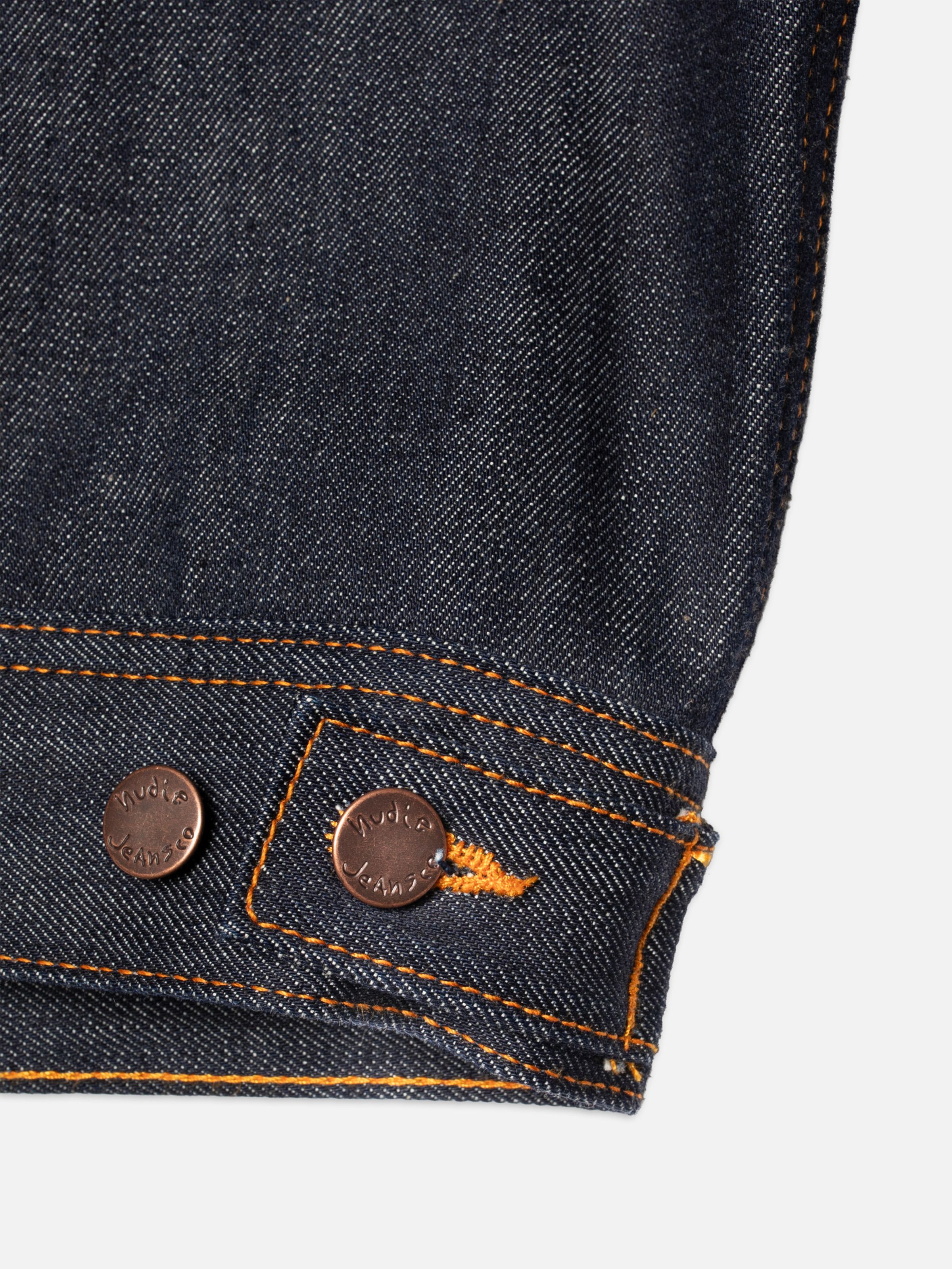 Nudie Jeans Conny Denim Jacket Dry One, close-up of the hem featuring copper logo buttons and orange contrast stitching.