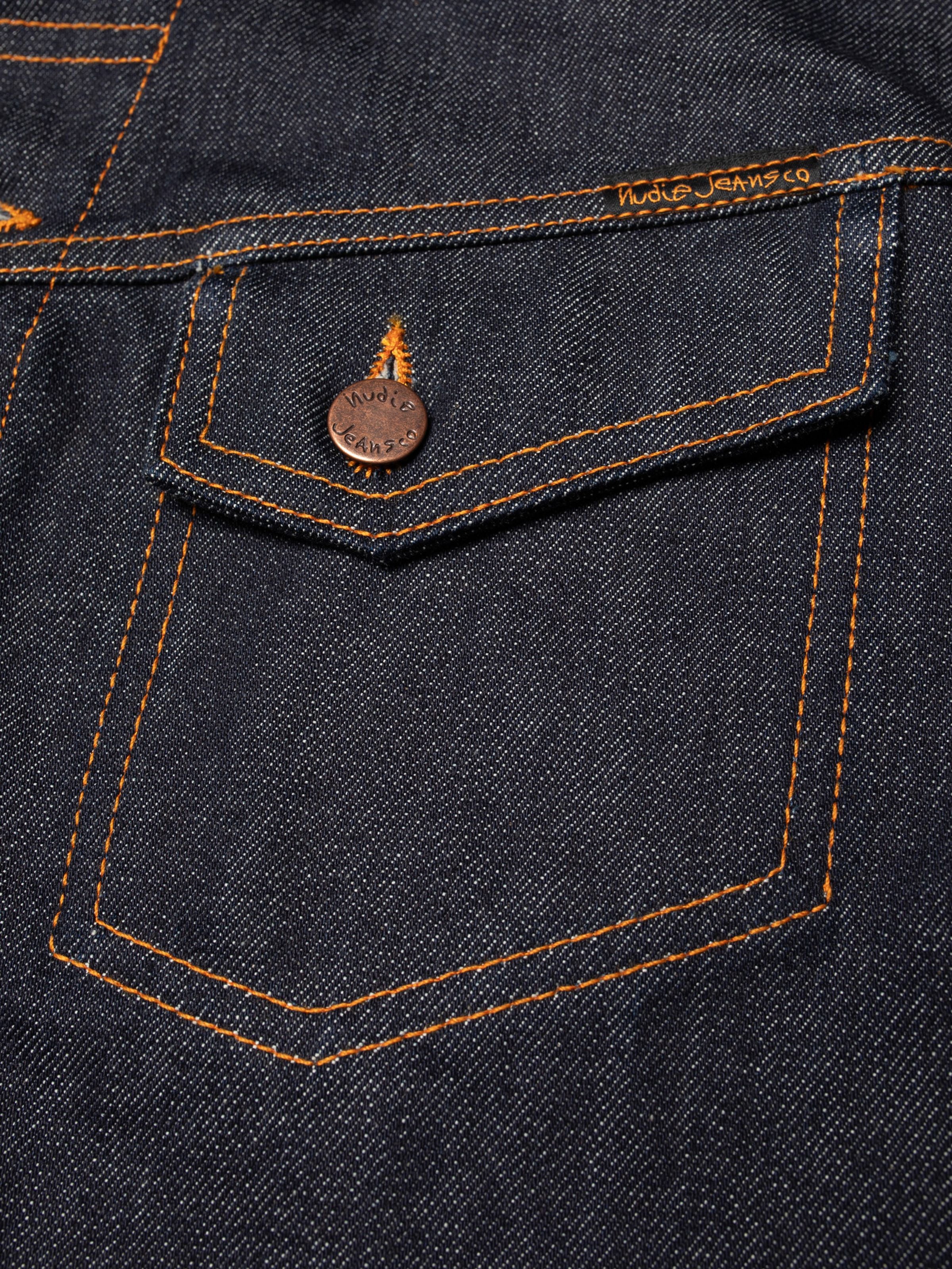 Nudie Jeans Conny Denim Jacket Dry One, chest pocket close-up in dark indigo rigid organic cotton with orange stitching.