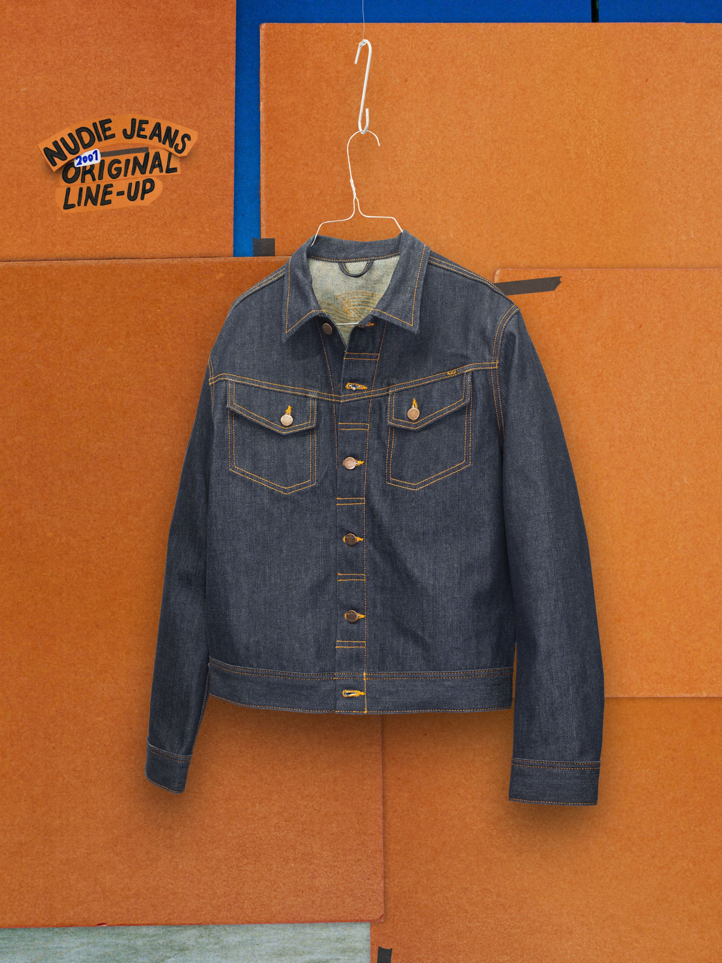Nudie Jeans Conny Denim Jacket Dry One, a slim-fit rigid denim jacket with orange stitching, hanging on a metal hanger.