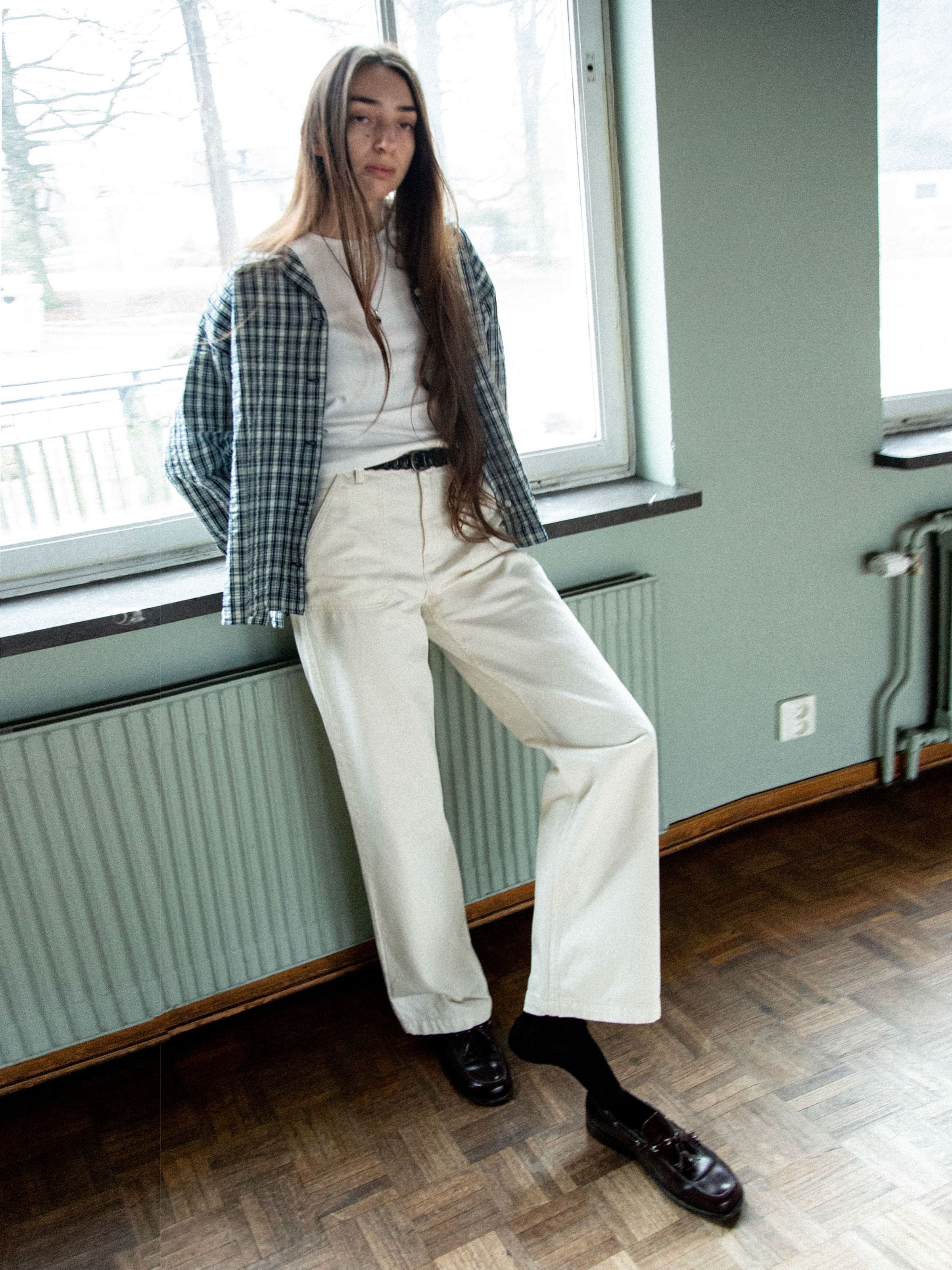 Nudie Jeans Asta Workwear Pants Ivory, Damenhose mit hohem Bund und weitem Bein an einem Model im Lifestyle-Setting gezeigt.
