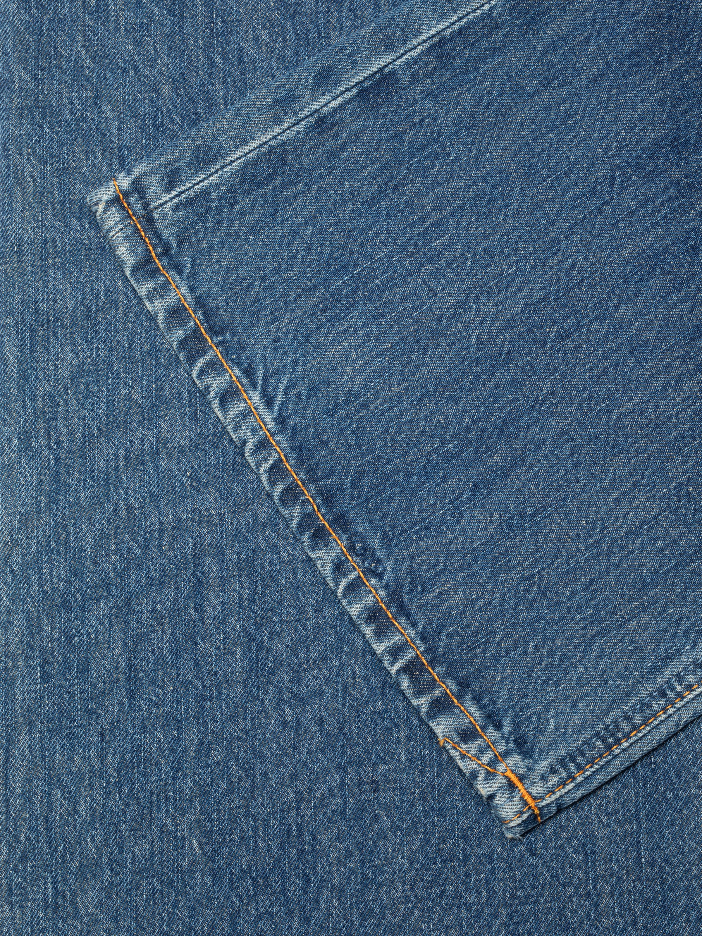 Nudie Jeans Dusty Dee Sierra Sun, close-up of the mid-blue rigid denim fabric with orange thread stitching.