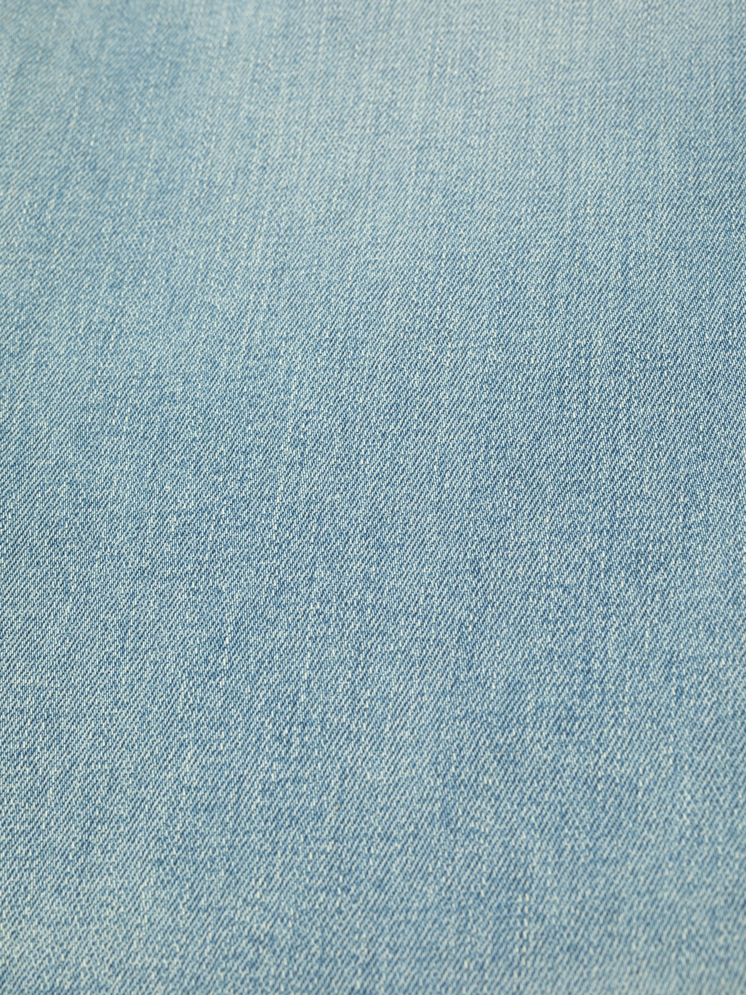 Nudie Jeans Grim Tim Shallow Waters, a close-up showing the texture of the pale light blue denim fabric.