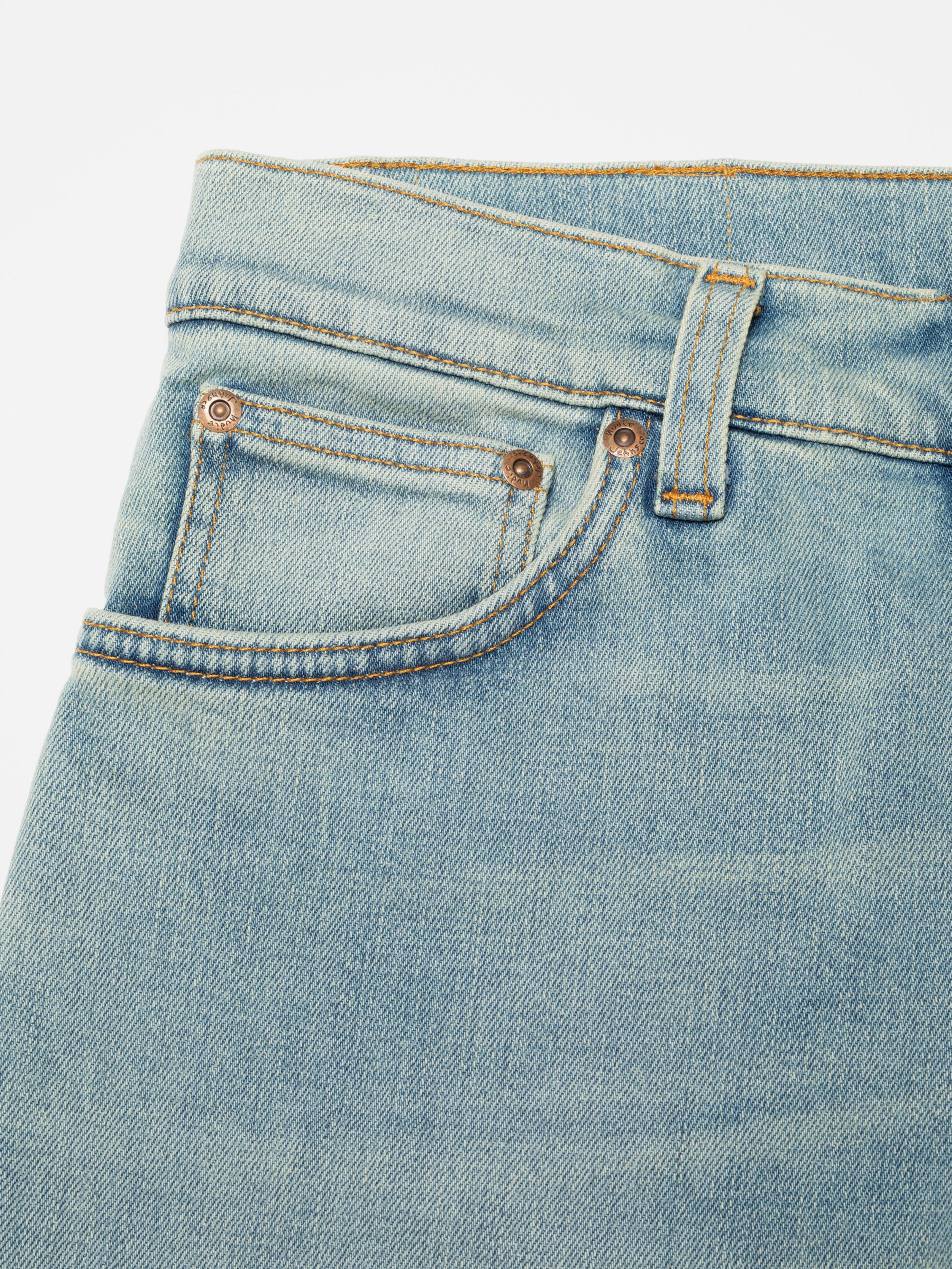 Nudie Jeans Grim Tim Shallow Waters, close-up of the front pocket and copper rivets on light blue denim.