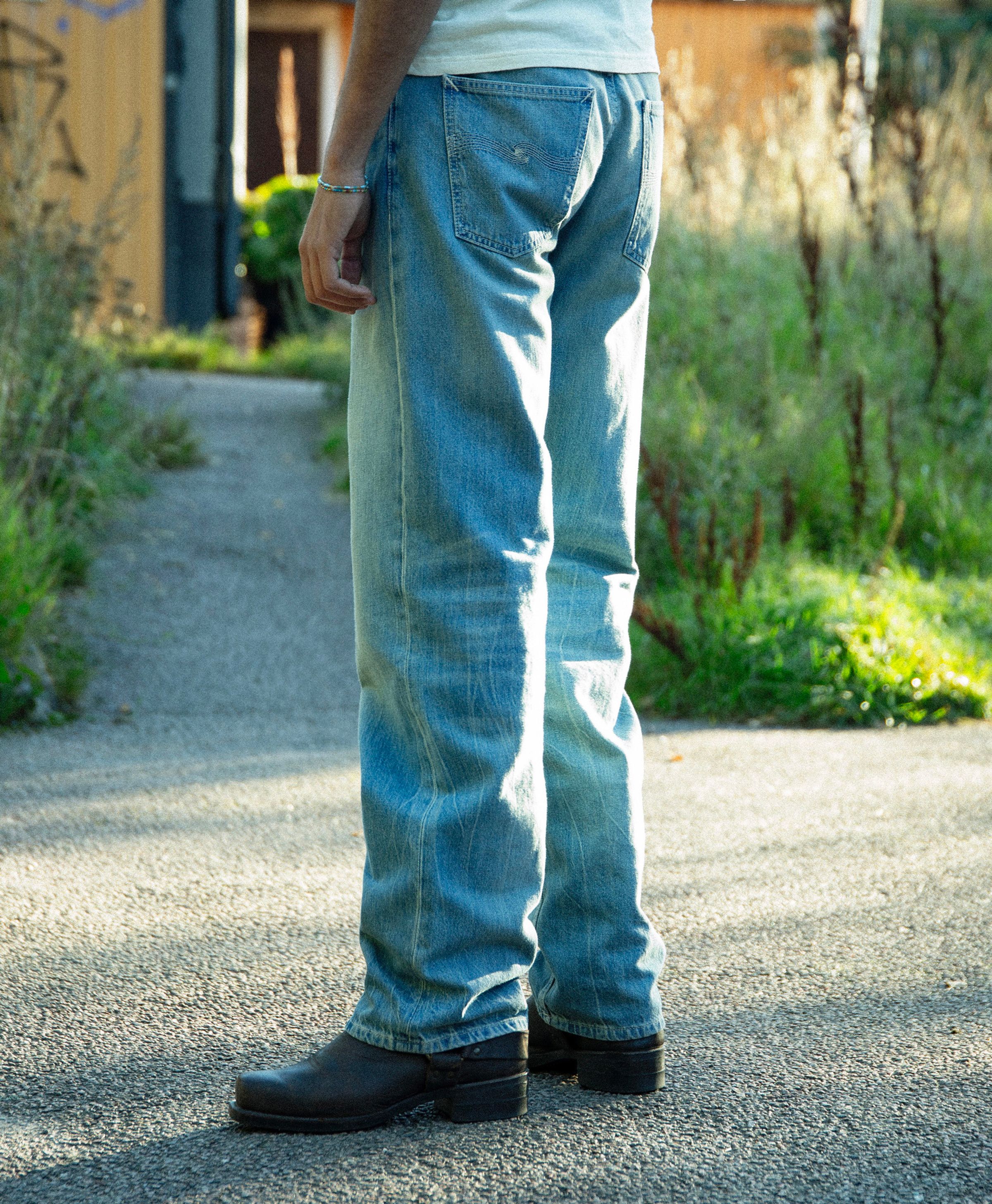 Nudie Jeans Tuff Tony Drift Wood, men's loose-fit wide-leg jeans shown from the back on a model in a lifestyle setting.