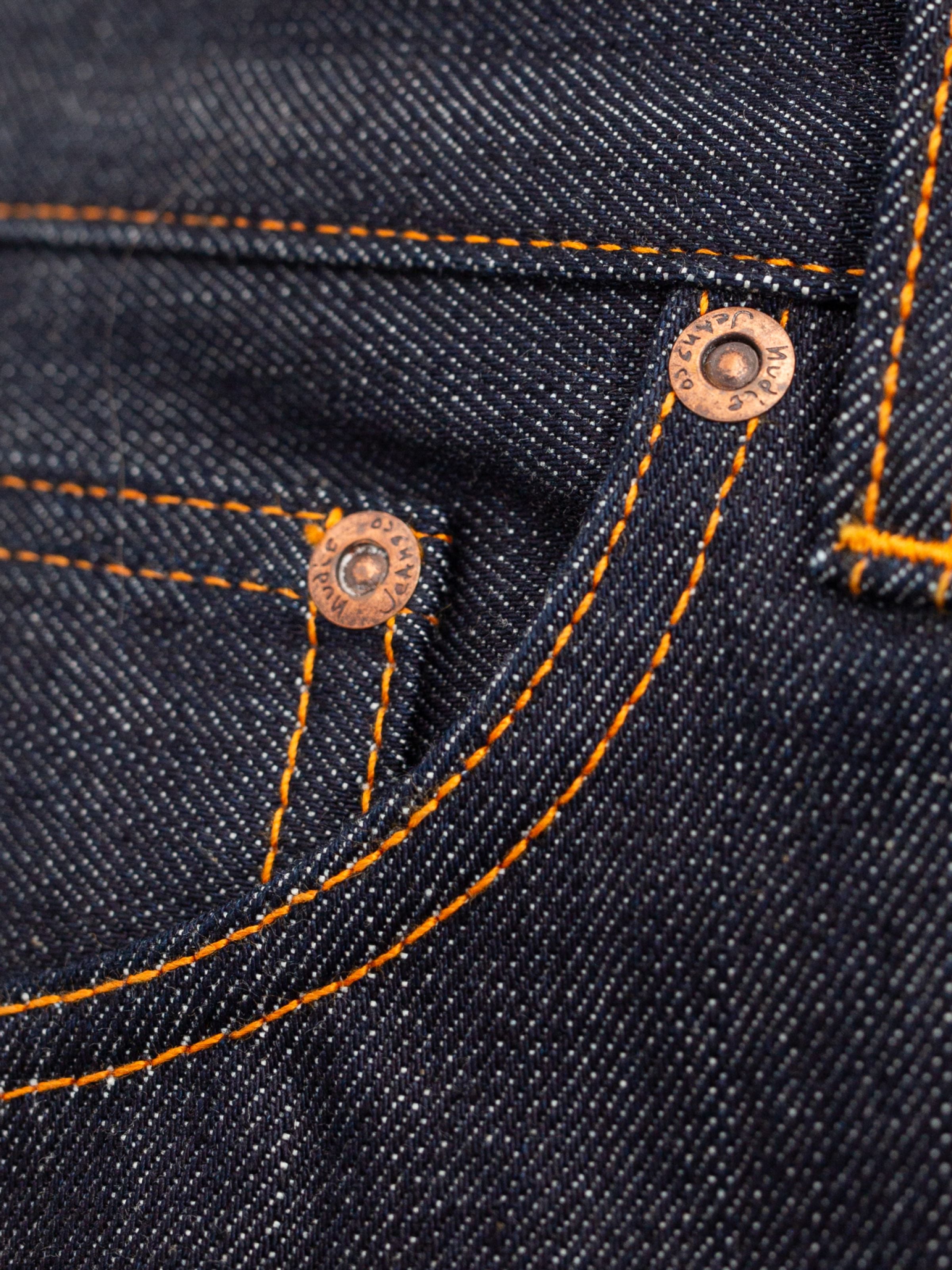 Nudie Jeans Flare Glenn Dry One, a close-up of the rigid organic cotton indigo denim, orange seams, and copper rivets.