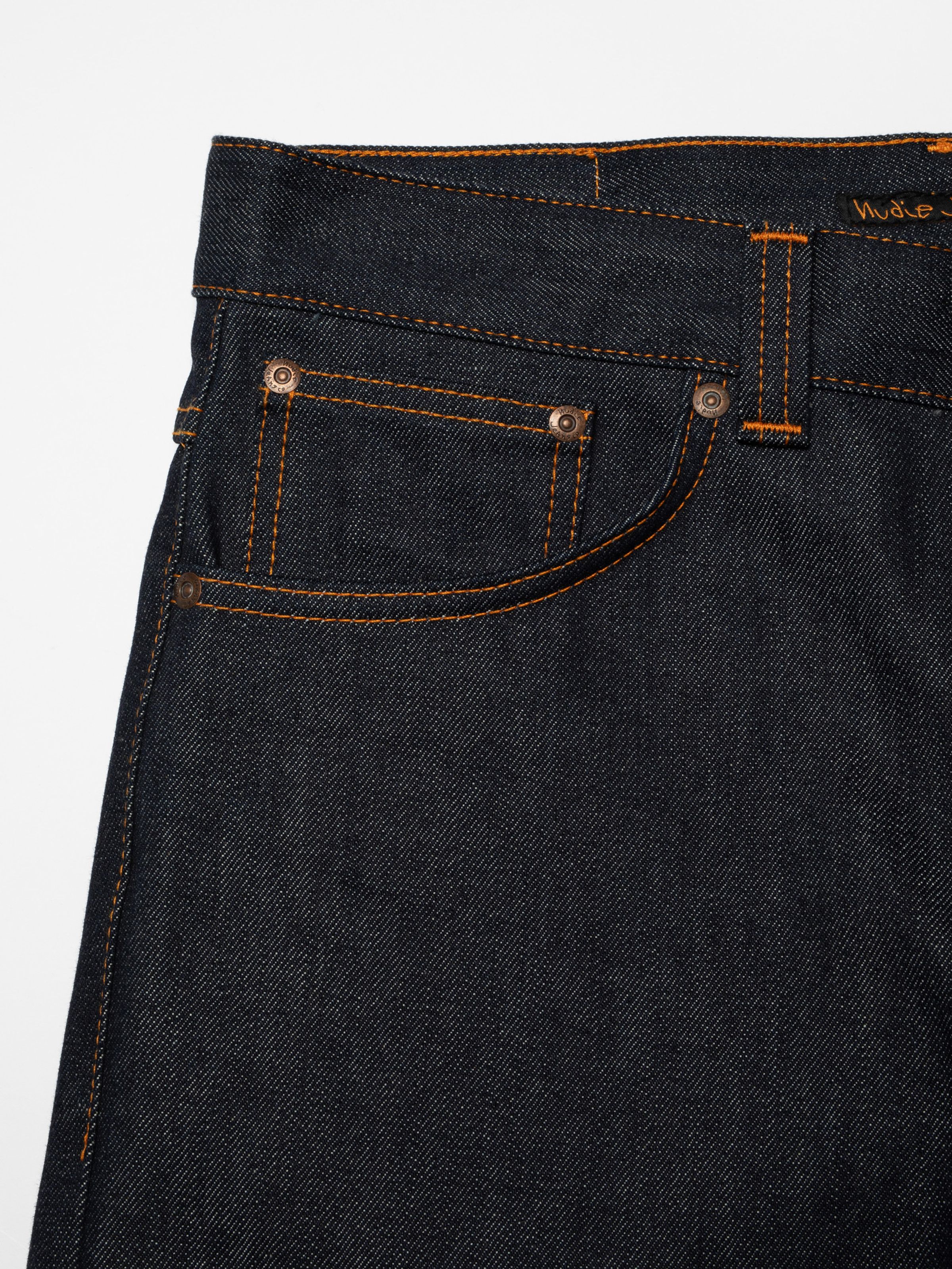 Nudie Jeans Flare Glenn Dry One, close-up of the front pocket area featuring orange stitching and copper trims.