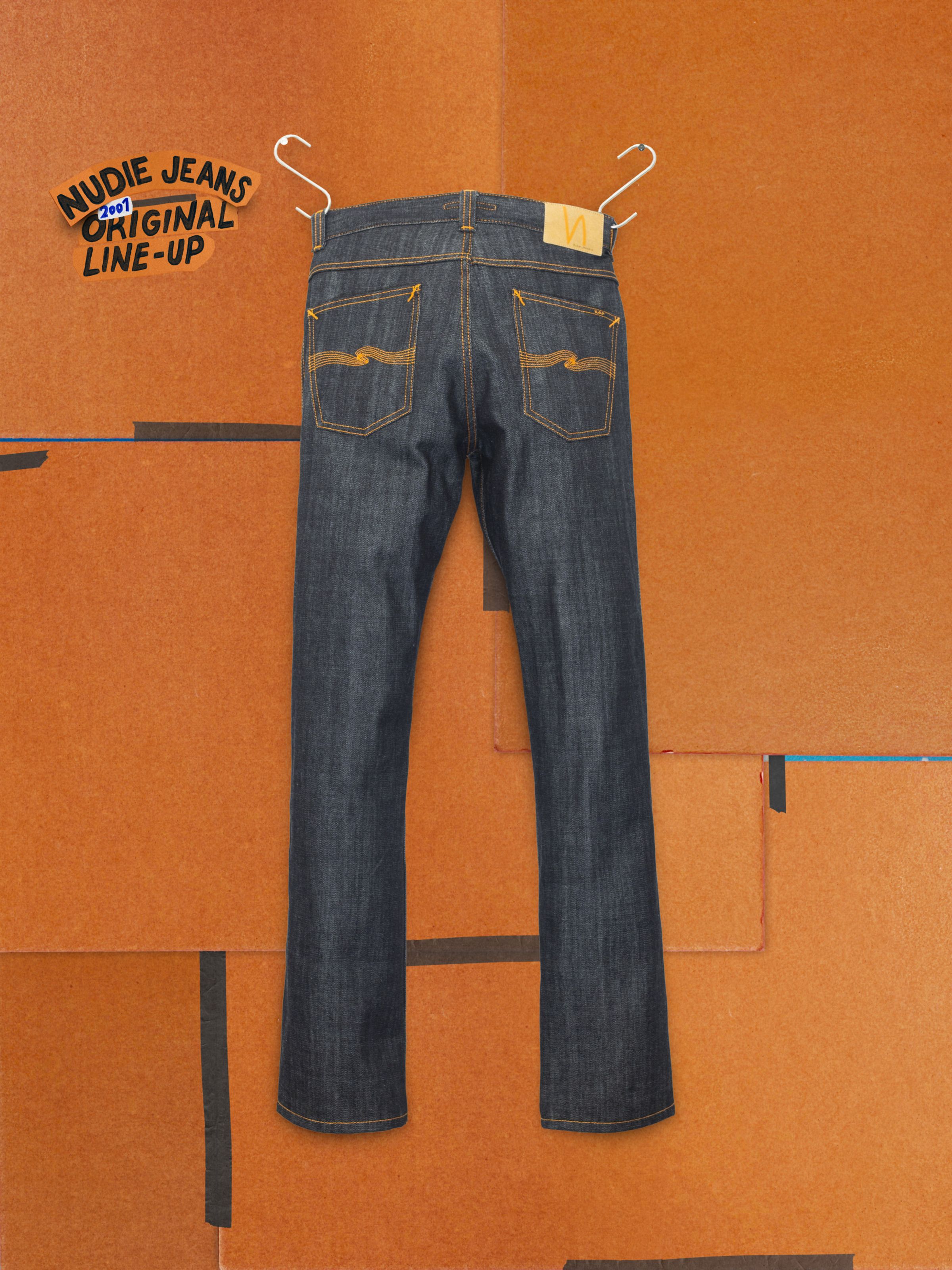 Nudie Jeans Slim Jim Dry Two, slim straight jeans in rigid dry blue denim, back view hanging on an orange backdrop.