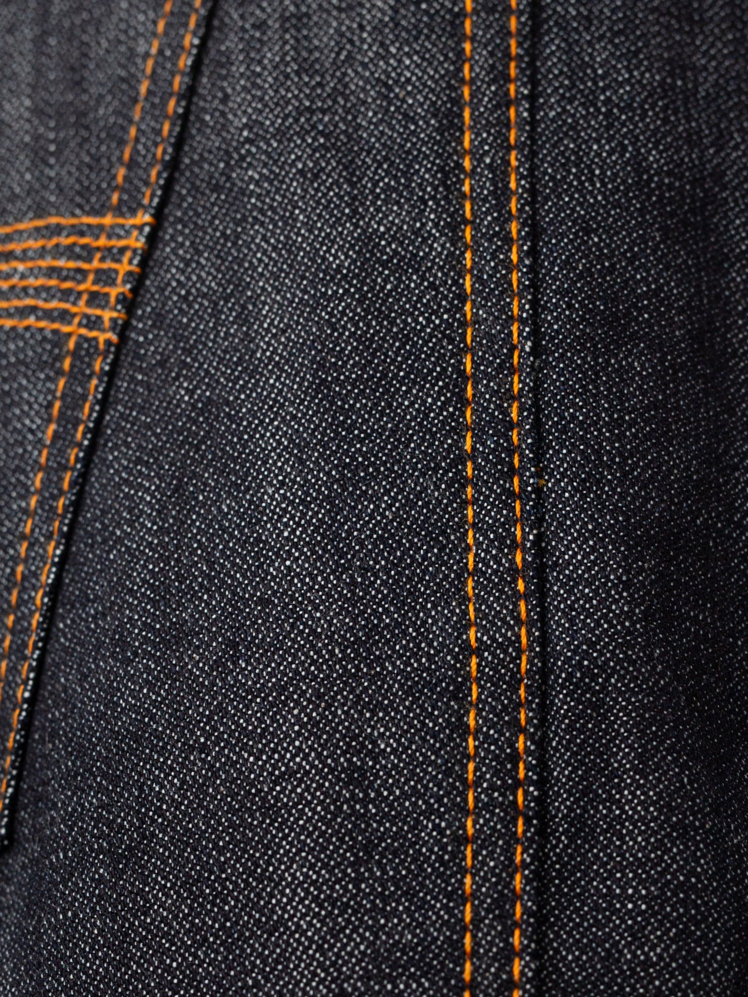 Nudie Jeans Slim Jim Dry Two, a close-up of the rigid organic cotton denim fabric with orange contrast stitching.