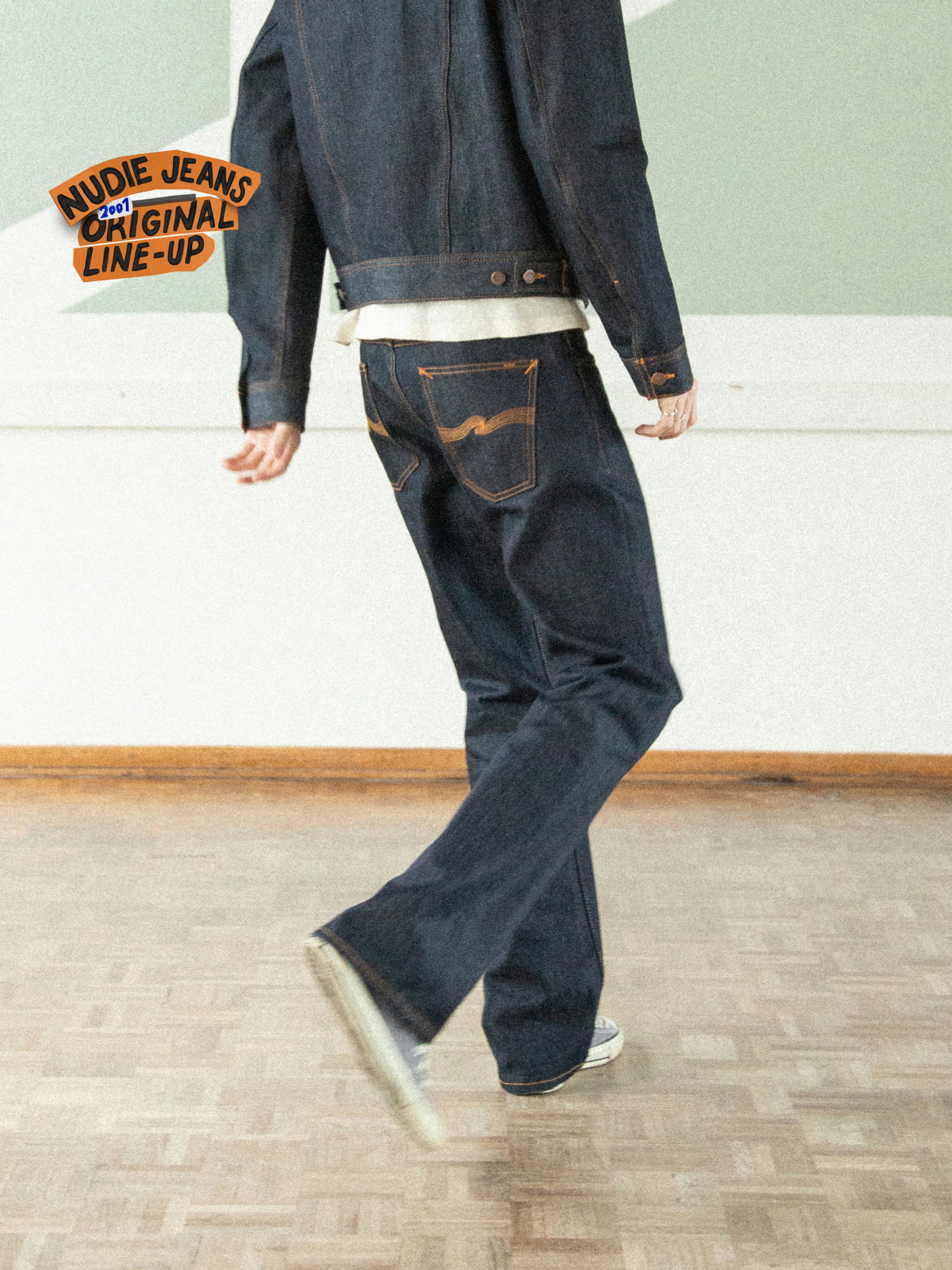 Nudie Jeans Regular Alf Dry One, men's bootcut jeans in dry blue rigid denim, shown from behind on a walking model.