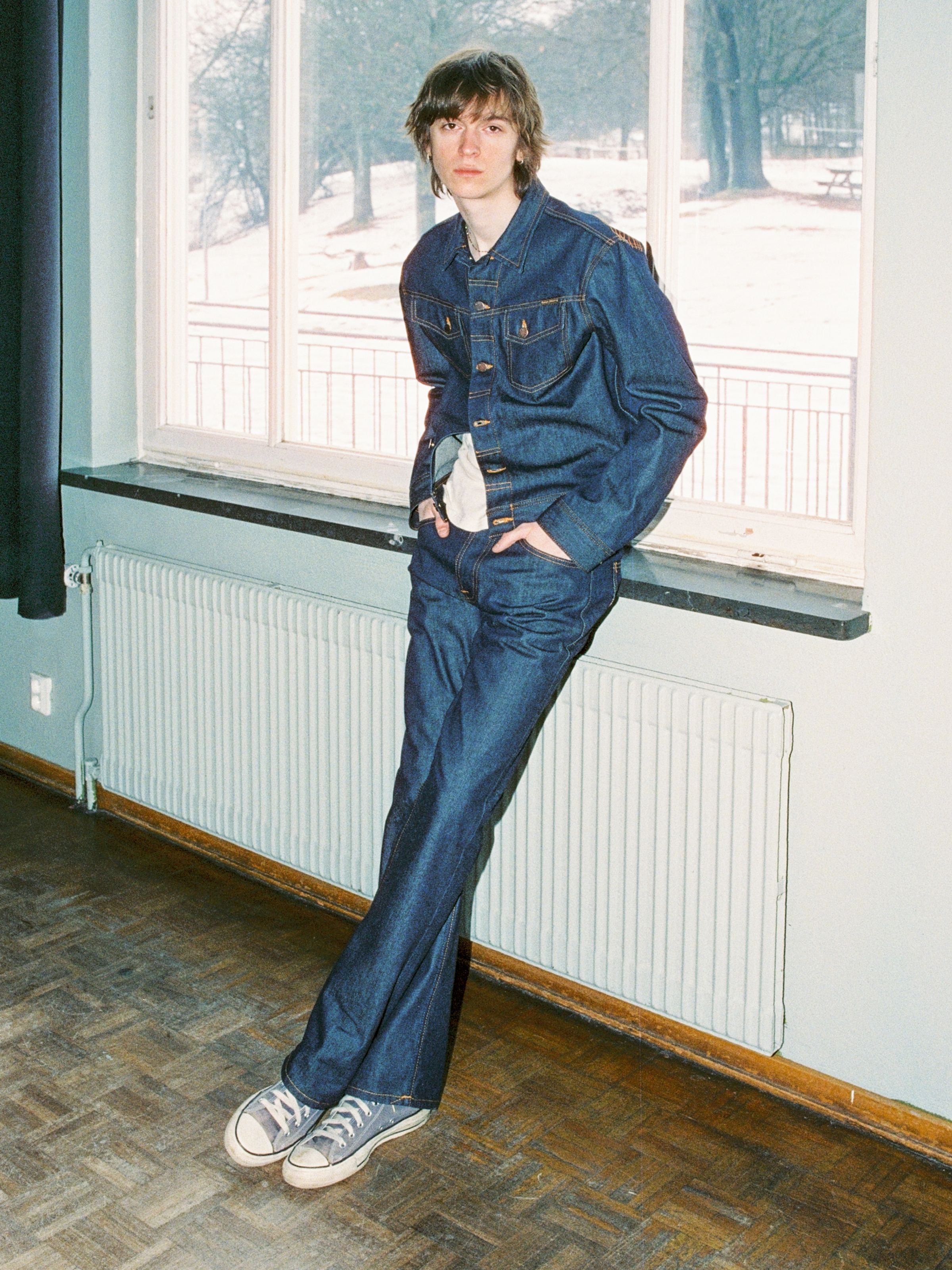 Nudie Jeans Regular Alf Dry One, men's regular-fit bootcut jeans shown on a model leaning against a windowsill.