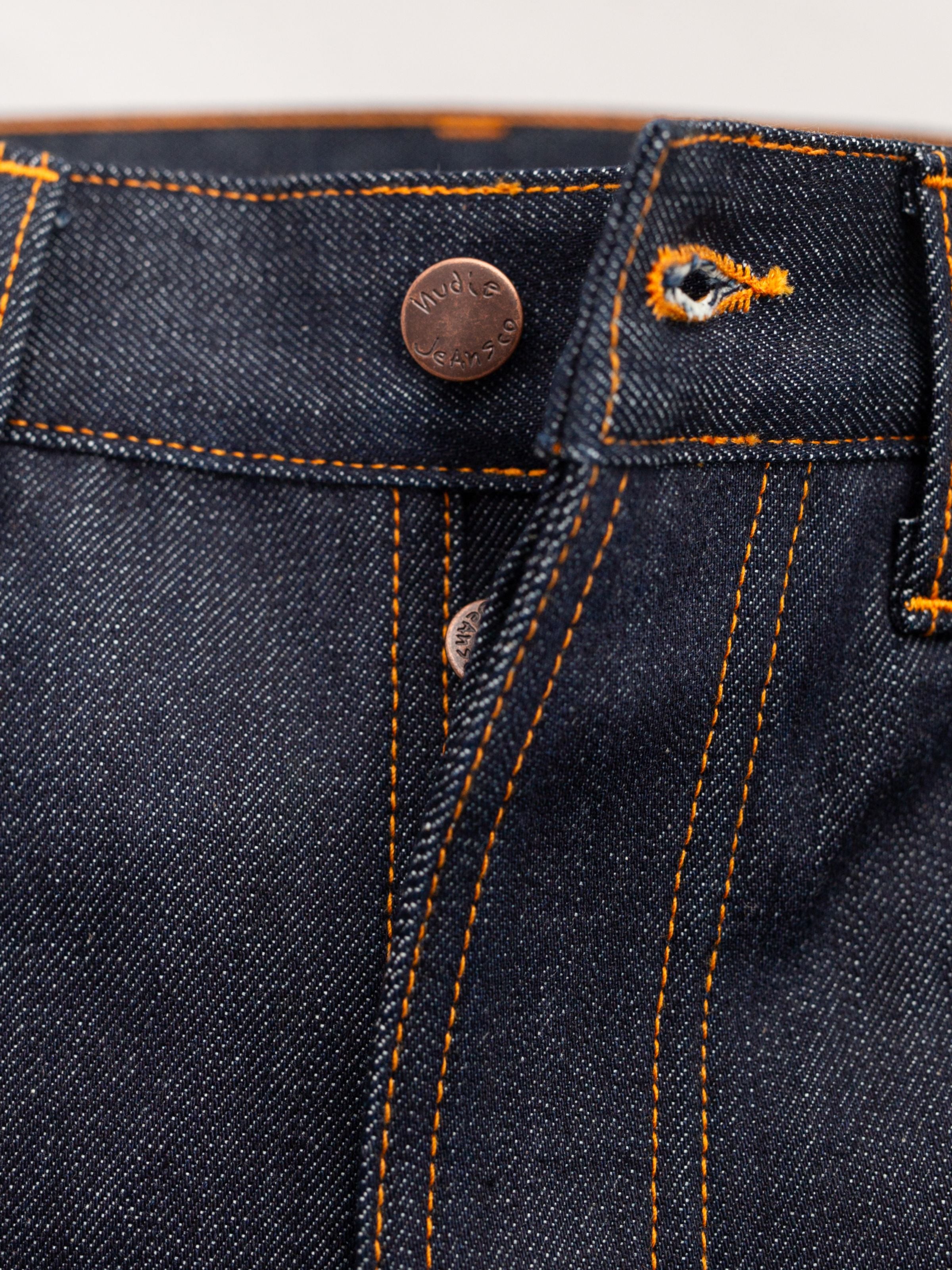Nudie Jeans Regular Alf Dry One, a close-up of the copper button fly and orange stitching on rigid organic cotton denim.