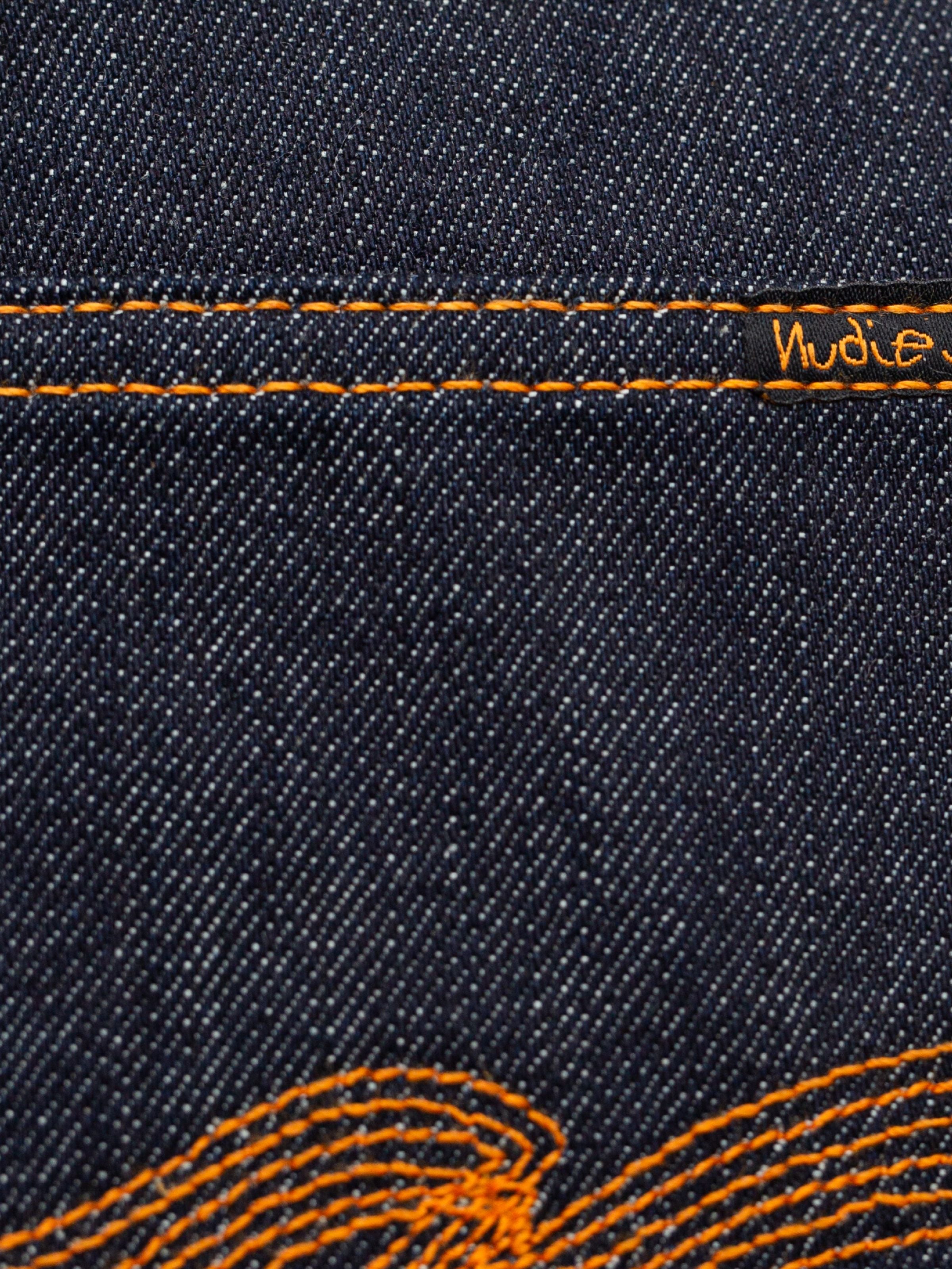 Nudie Jeans Regular Alf Dry One, a close-up of the dark indigo rigid organic cotton denim with orange thread stitching.
