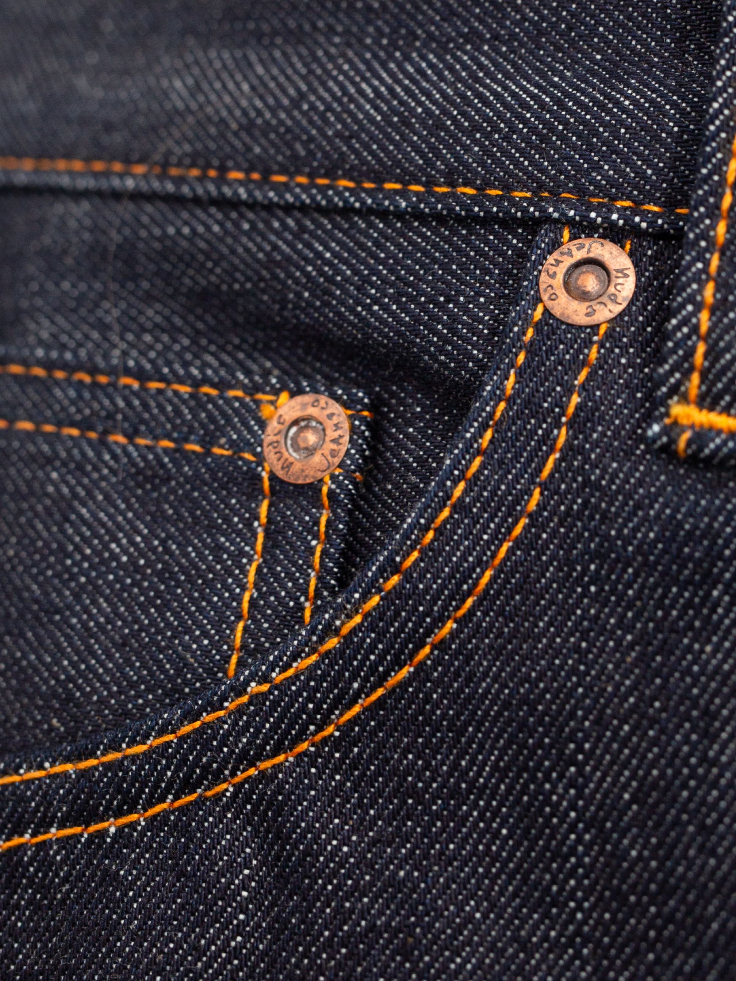 Nudie Jeans Regular Alf Dry One, a close-up of the organic cotton rigid denim with orange stitching and copper trims.