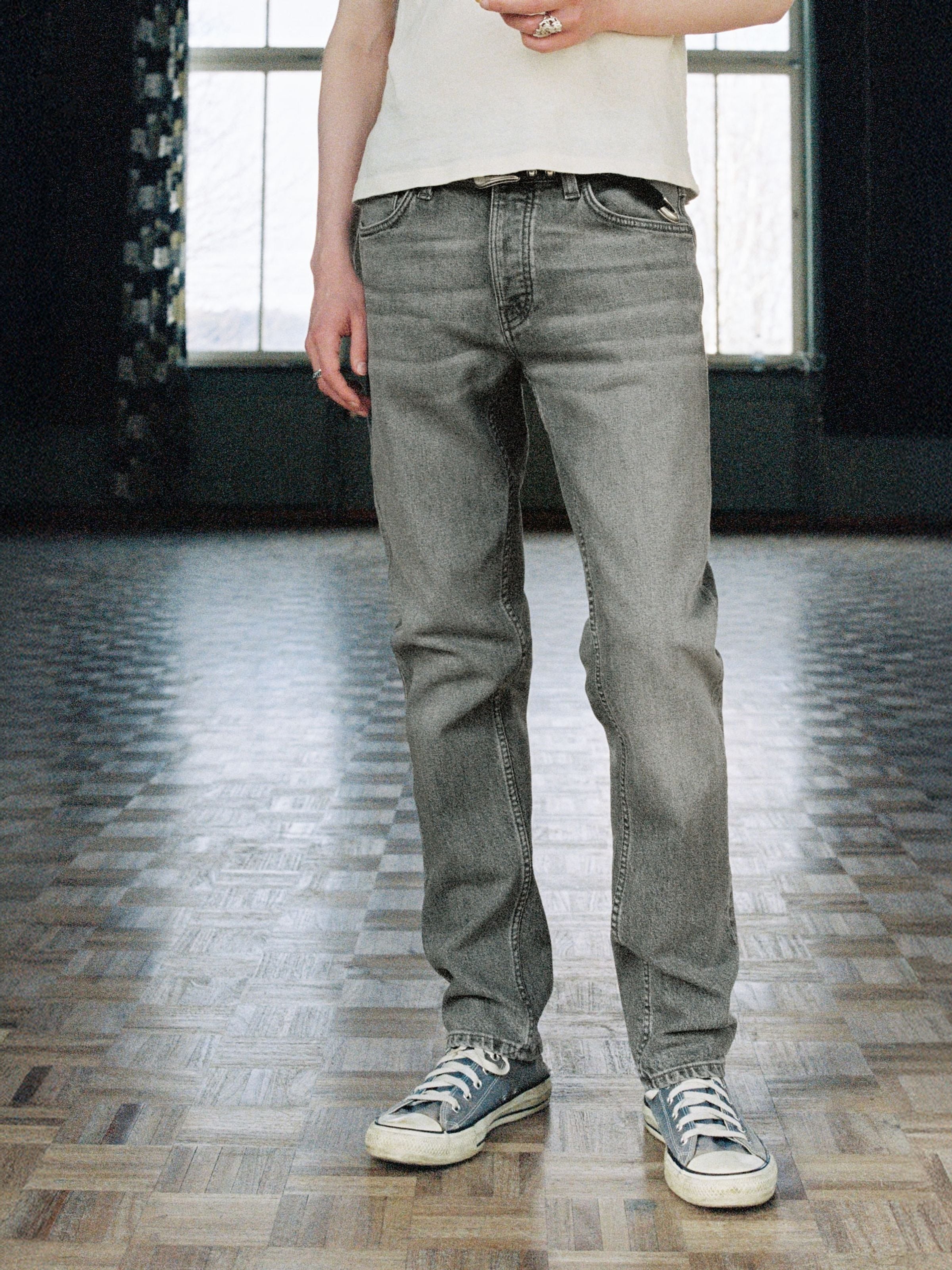 Nudie Jeans Solid Ollie Pale Ash, Herrenjeans, schmale Passform, hellgraue Waschung, von der Taille abwärts am Model gezeigt.