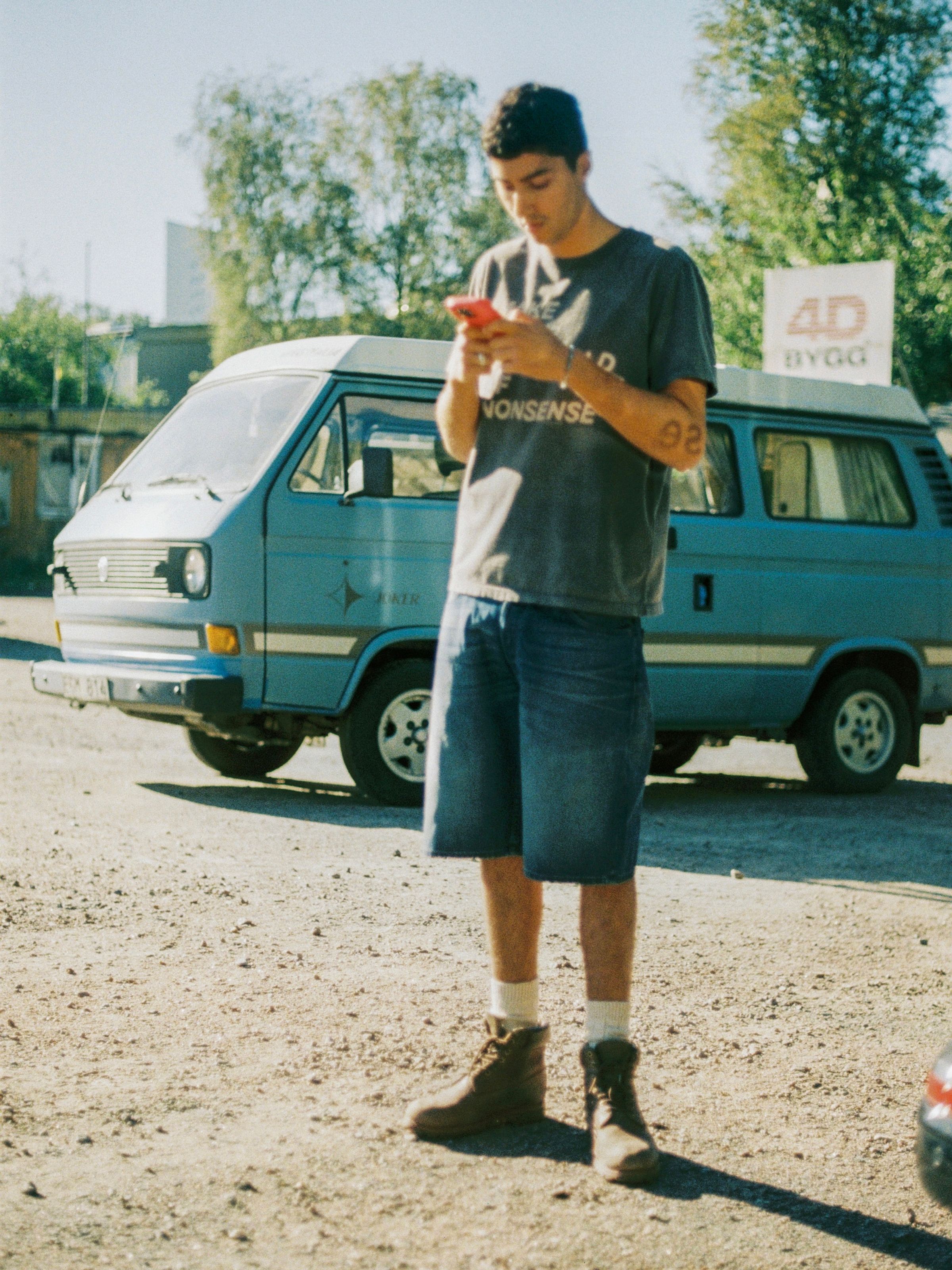 Nudie Jeans Zeb Denim Shorts Blue Painter, men's loose fit shorts shown on a model in front of a blue van.