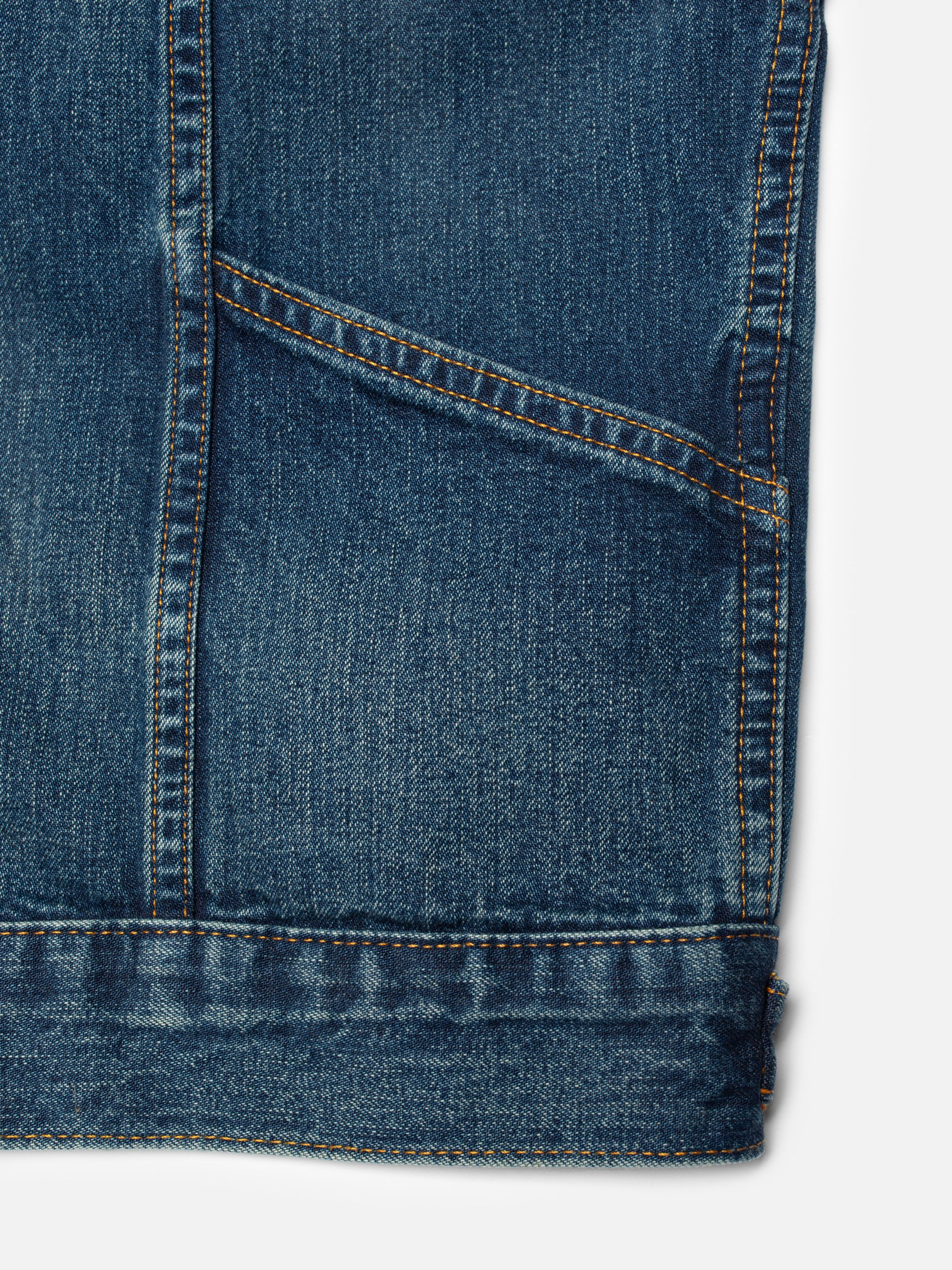 Nudie Jeans Britta Jacket Orange Painter, close-up of the mid blue denim fabric, pocket, and orange contrast stitching.
