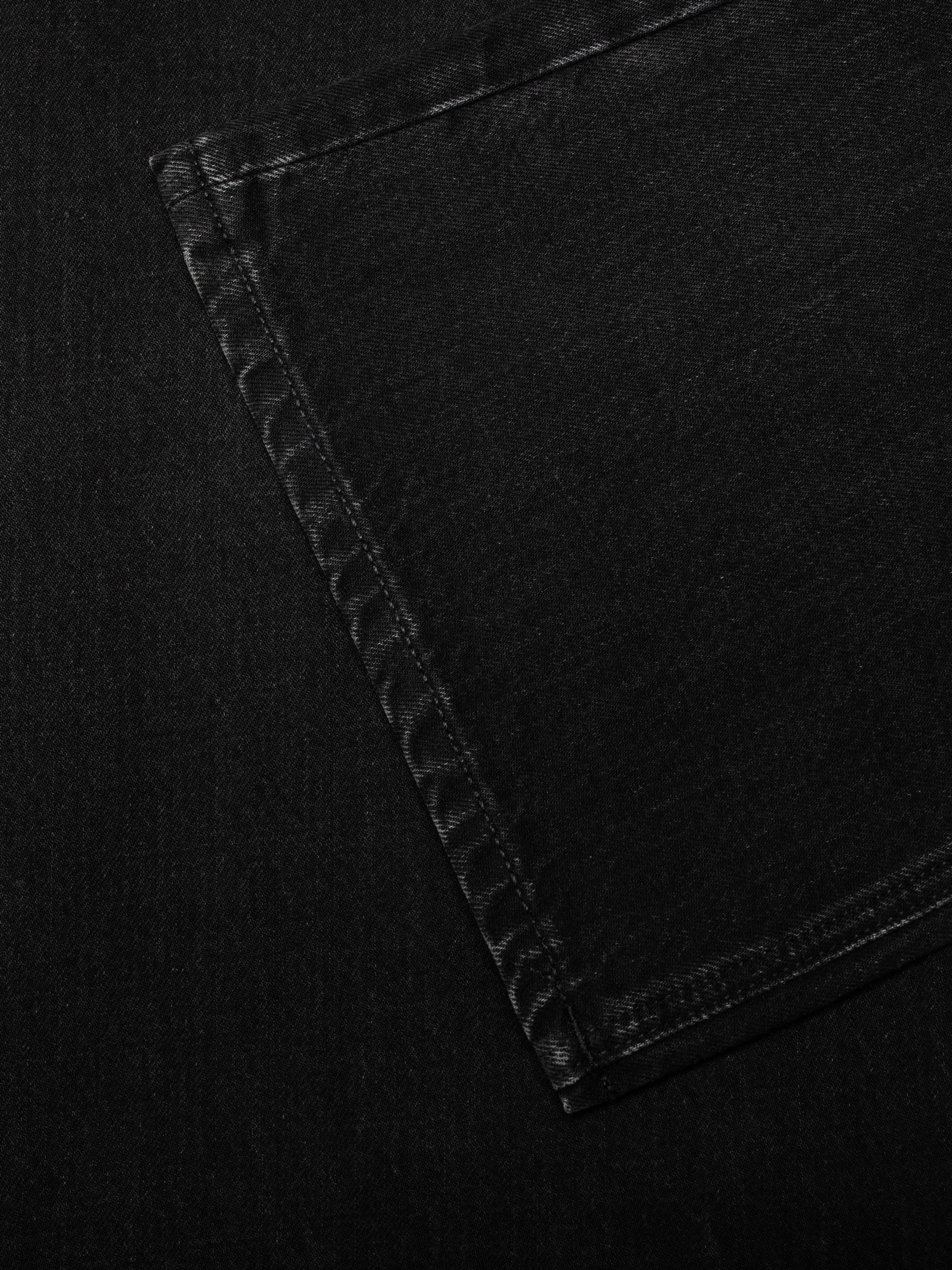 Nudie Jeans Dusty Dee Night Dune, women's flared jeans, showing a close-up of the back pocket and rigid black denim texture.