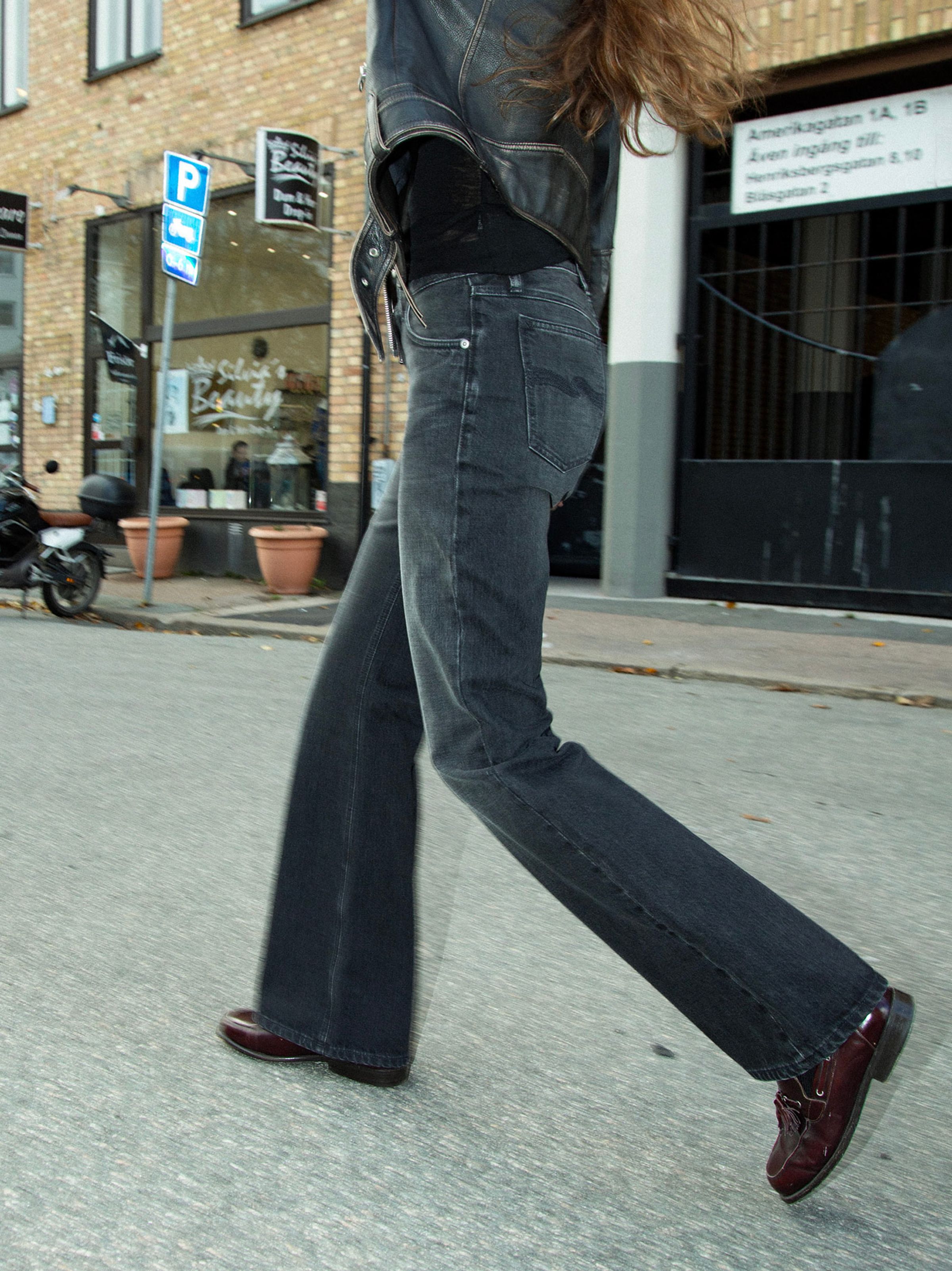 Nudie Jeans Dusty Dee Night Dune, women's flared leg jeans, shown on a model walking down a street.
