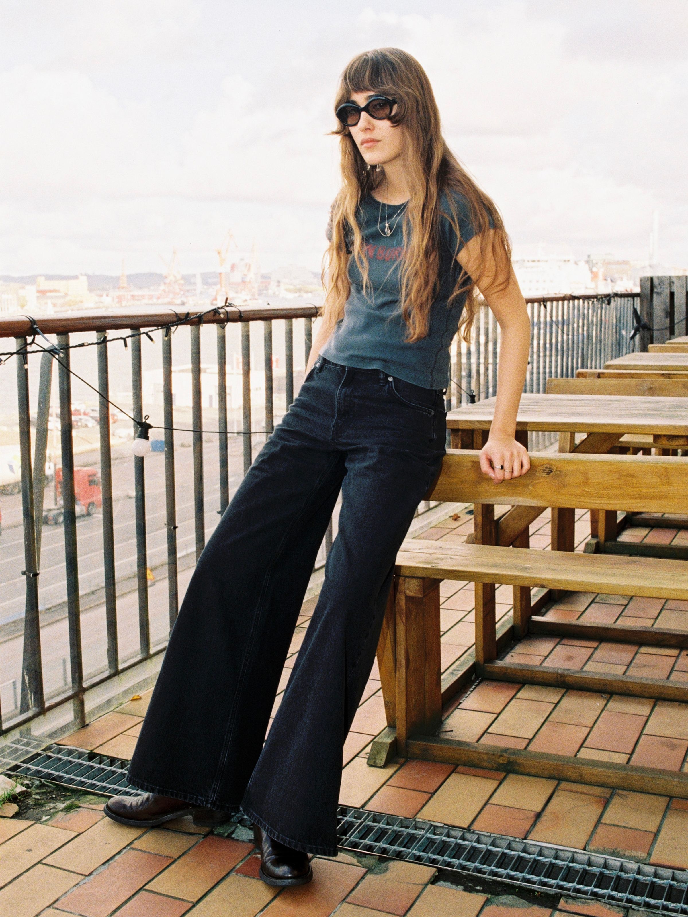 Nudie Jeans Sonic Sue Friendly Black, Damenjeans mit weitem A-Linien-Bein, von einem Model auf einer Terrasse getragen.
