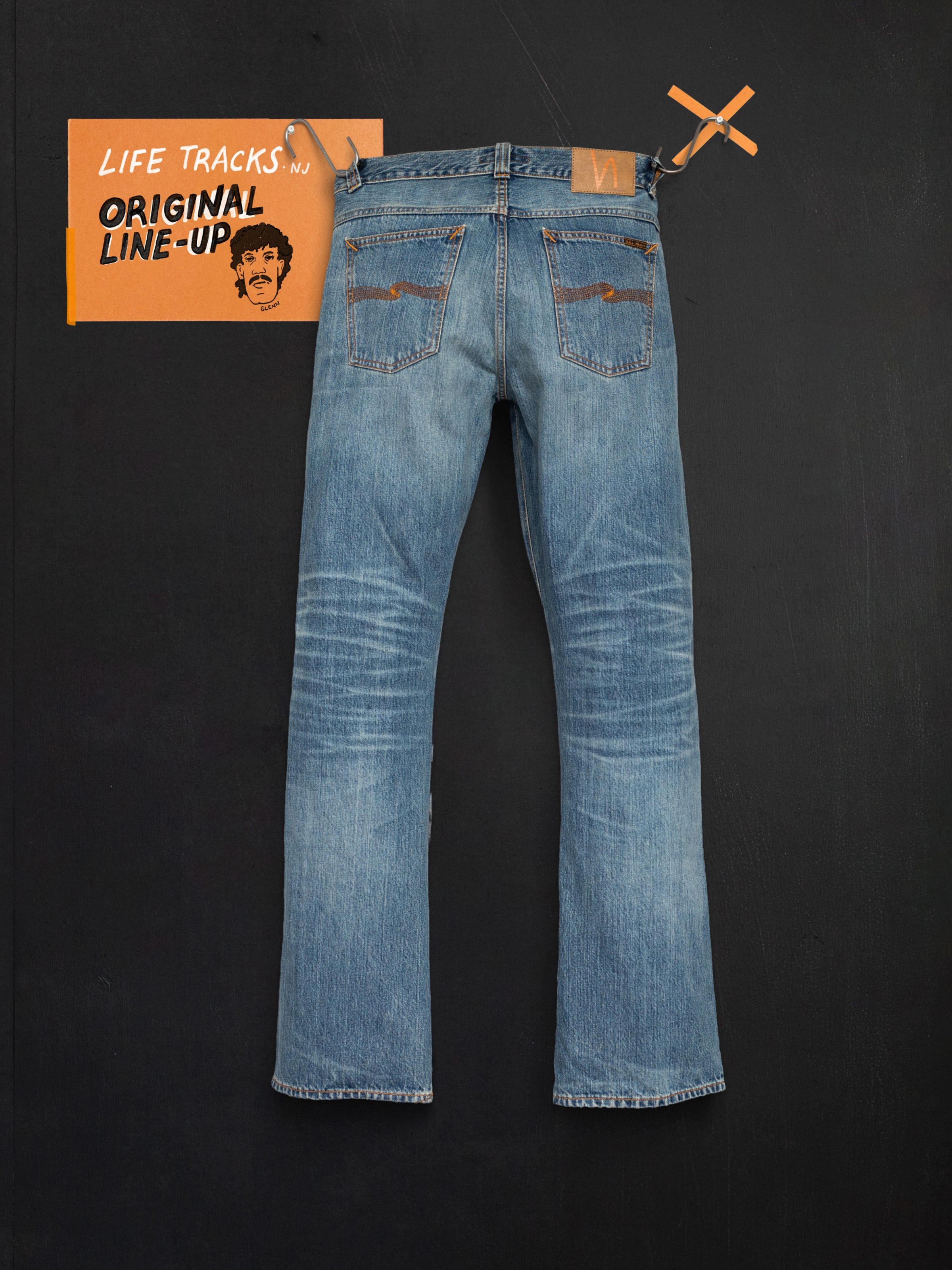 Nudie Jeans Regular Alf Silver Tracks bootcut jeans in mid blue wash with authentic fades, back view on a dark wall.