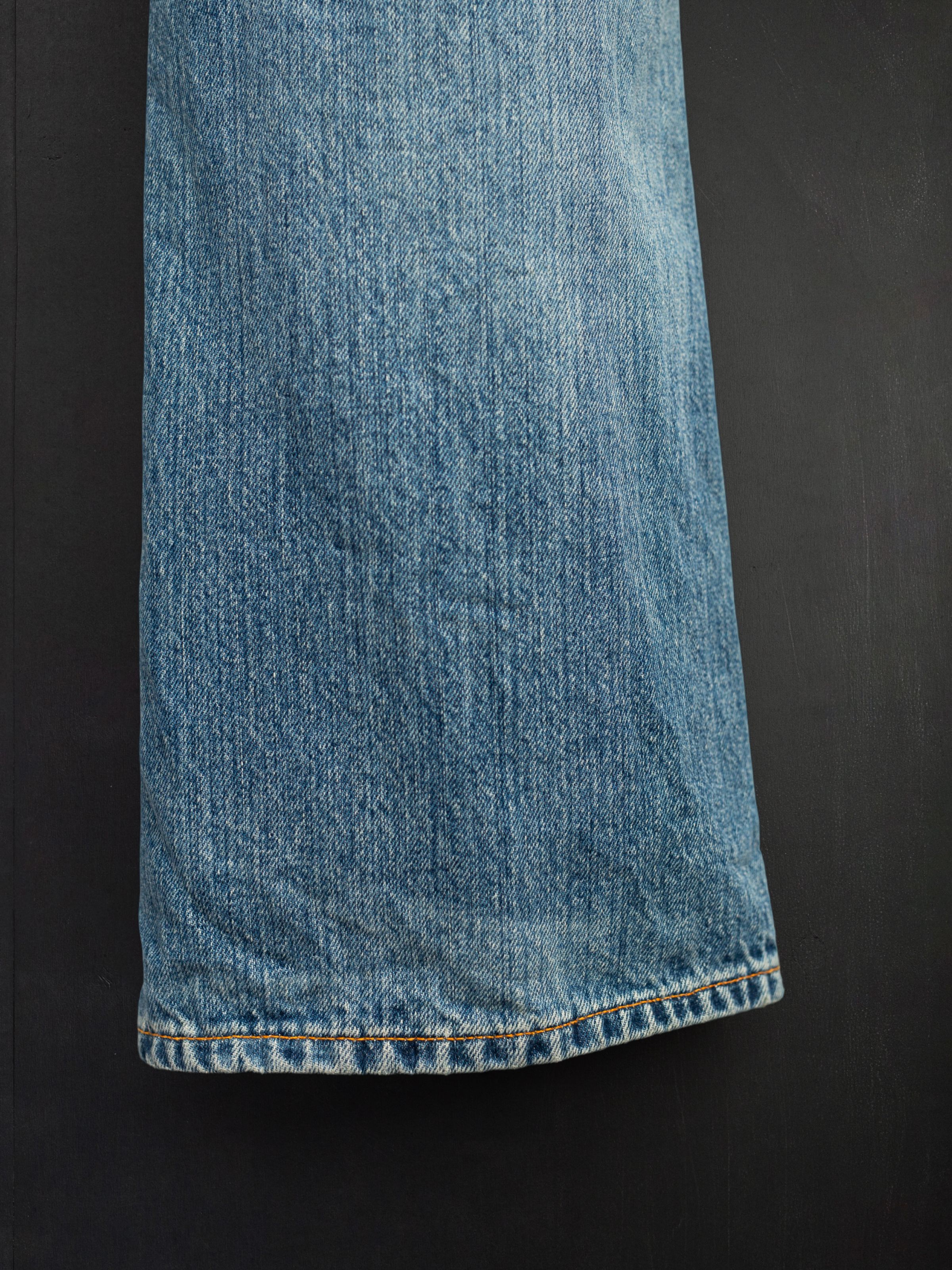 Nudie Jeans Regular Alf Silver Tracks, close-up of the bootcut leg opening with orange stitching and mid blue denim.