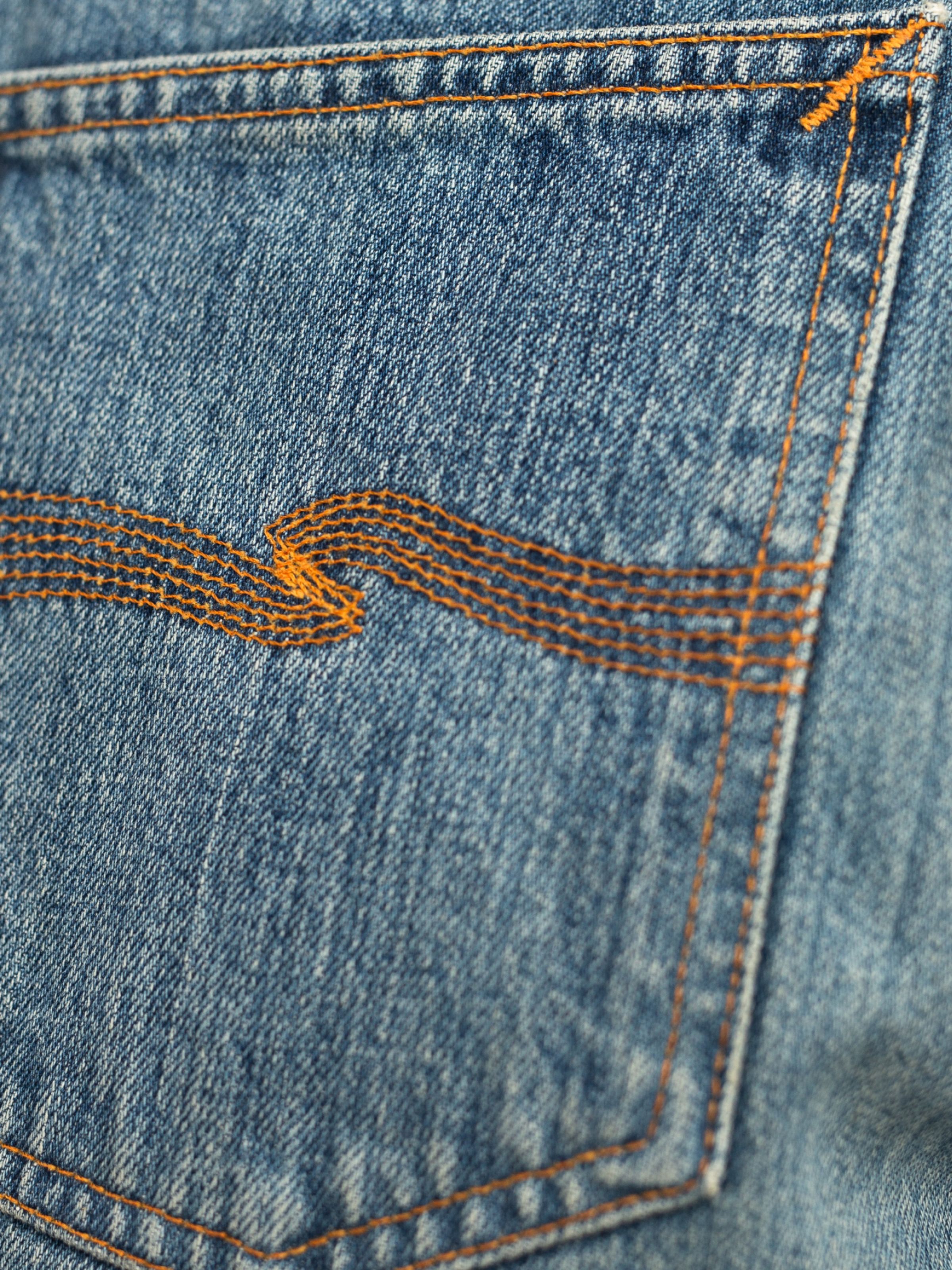 Nudie Jeans Regular Alf Silver Tracks, close-up of the signature orange back pocket embroidery on mid blue washed denim.