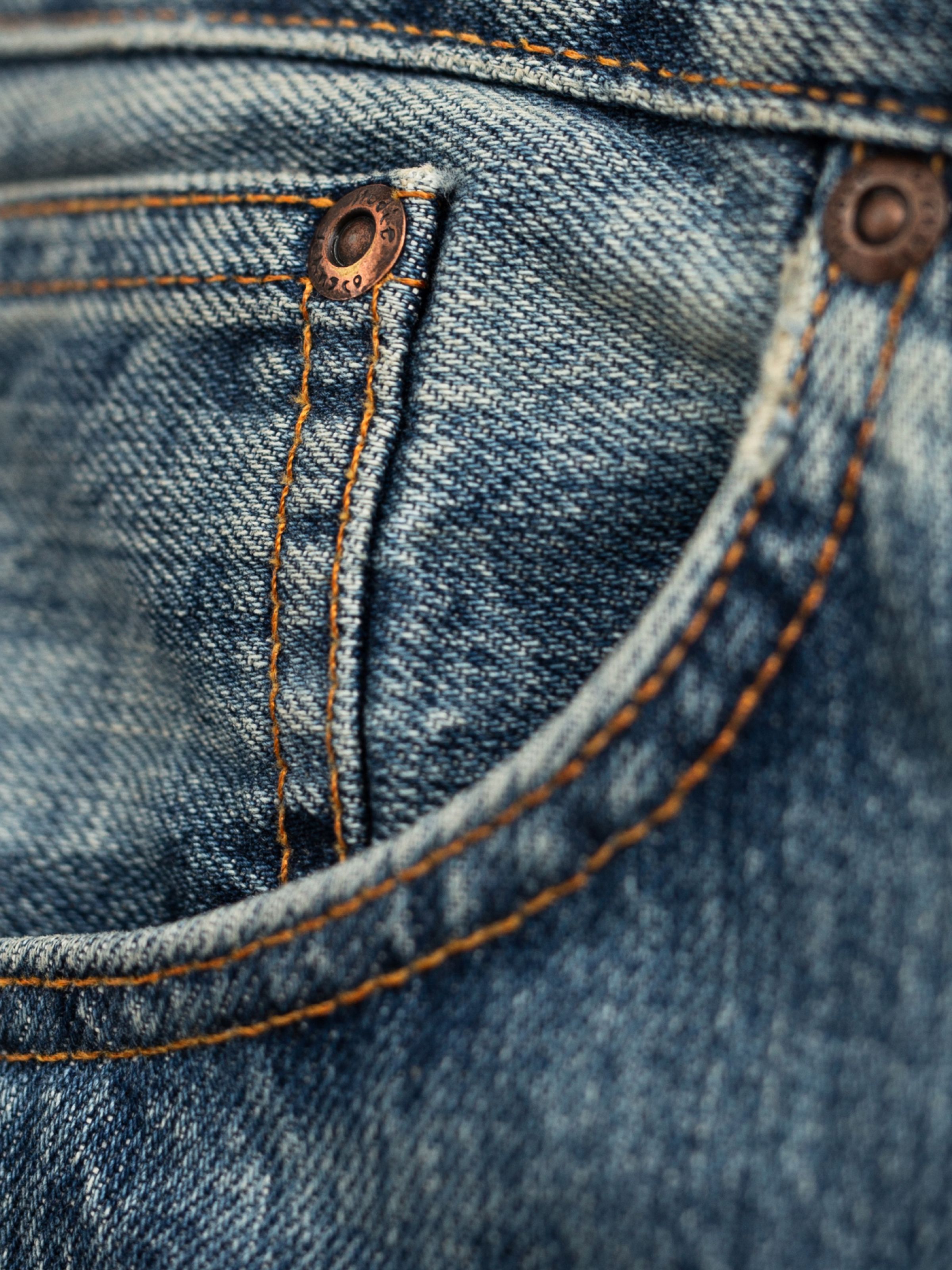 Nudie Jeans Regular Alf Silver Tracks, close-up of the front pocket with orange stitching and copper rivets.