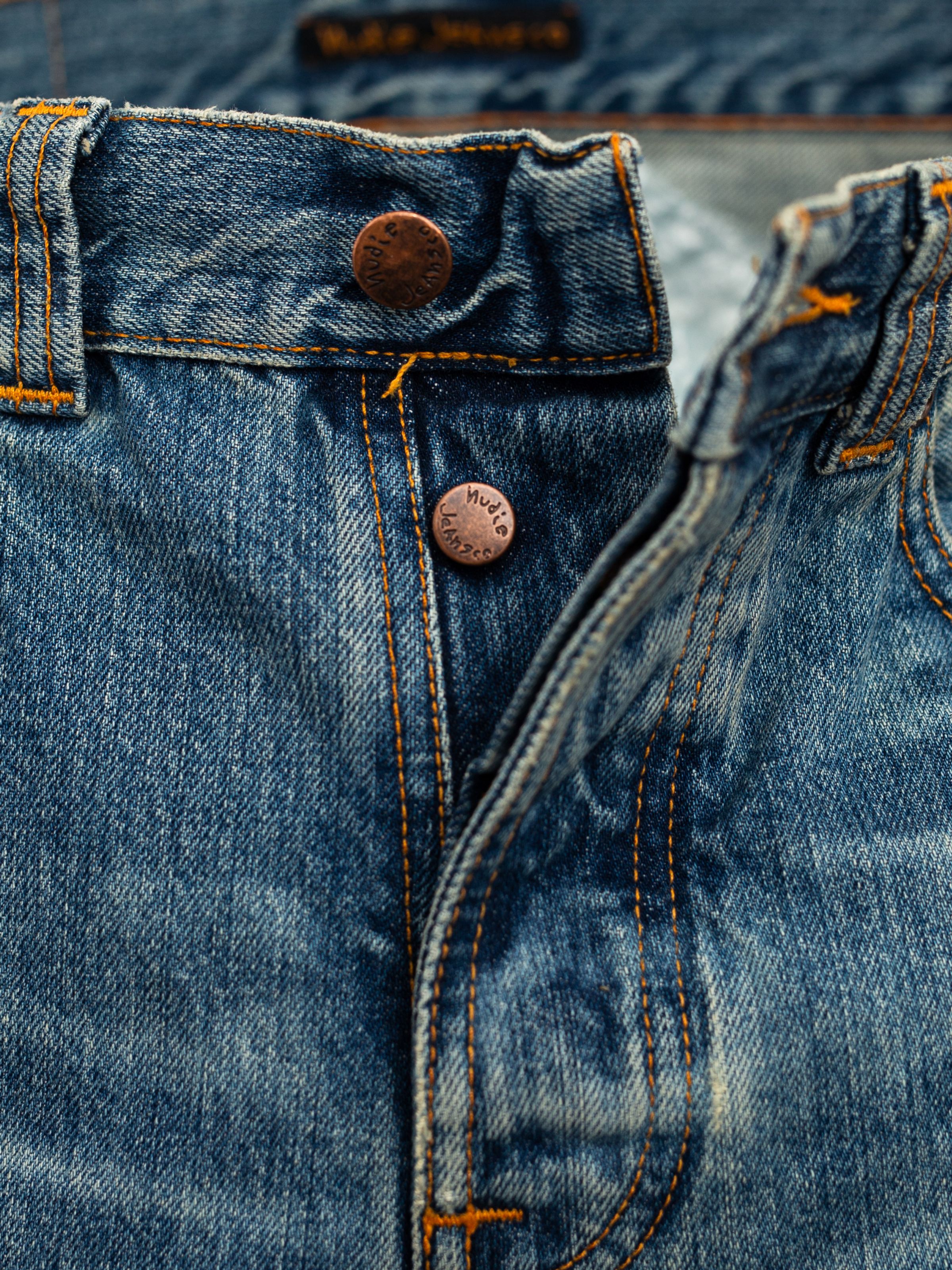Nudie Jeans Regular Alf Silver Tracks, close-up of the button fly featuring copper branded trims and orange thread.