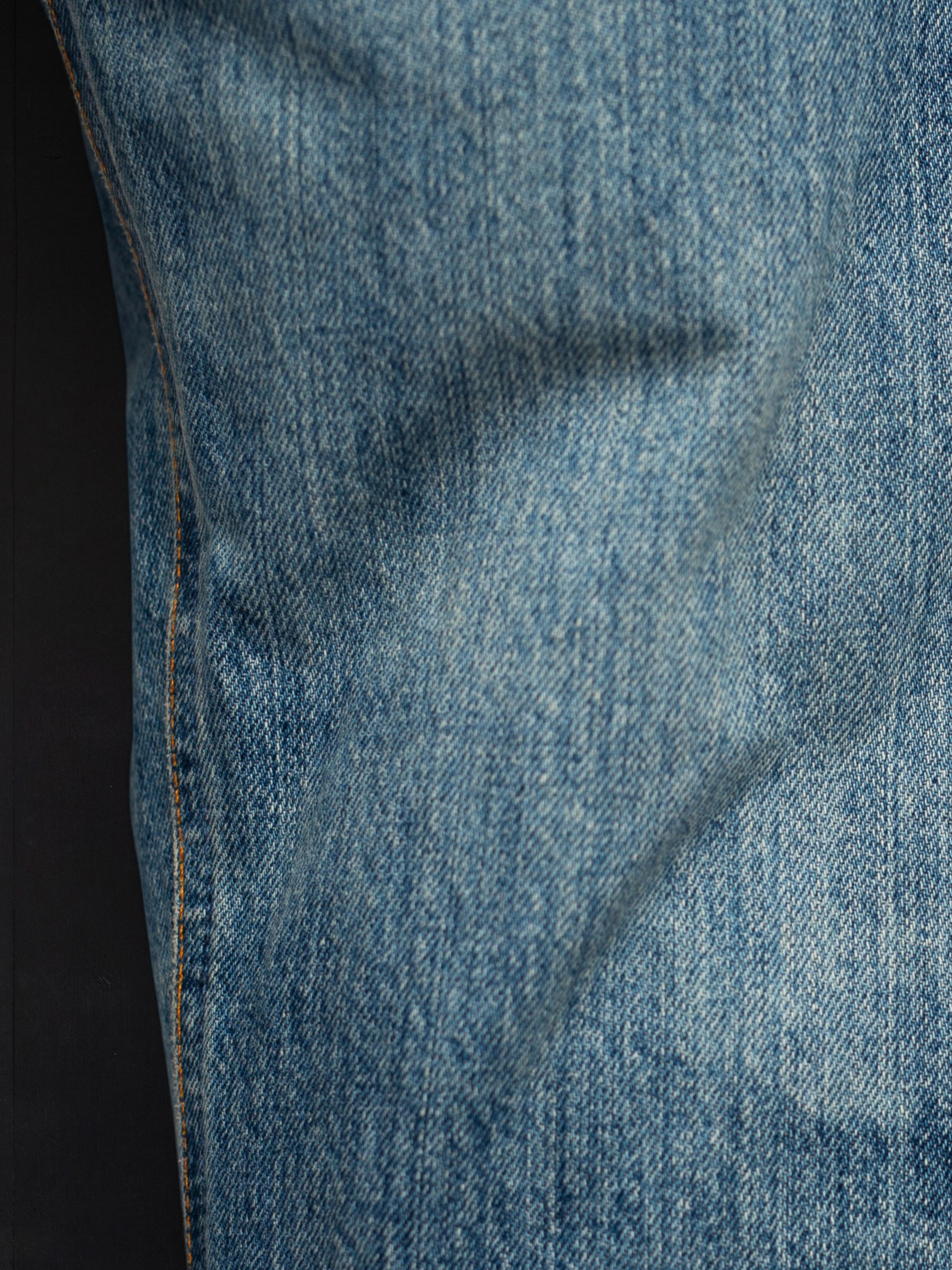 Nudie Jeans Regular Alf Silver Tracks, close-up of the mid blue washed denim fabric and orange stitching.