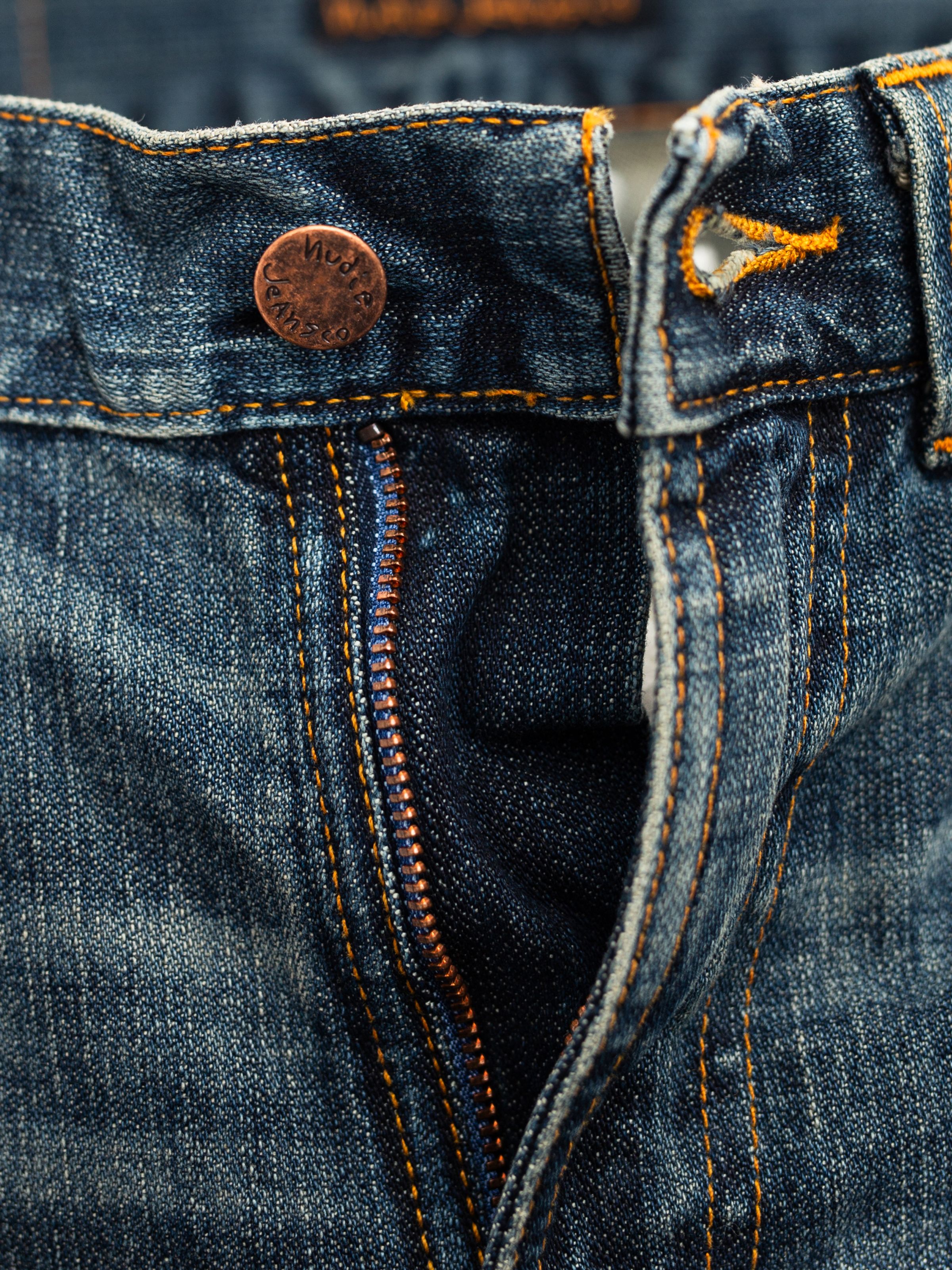 Nudie Jeans Slim Jim Quarter Tracks, close-up of the copper zip fly and orange stitching on washed blue denim.