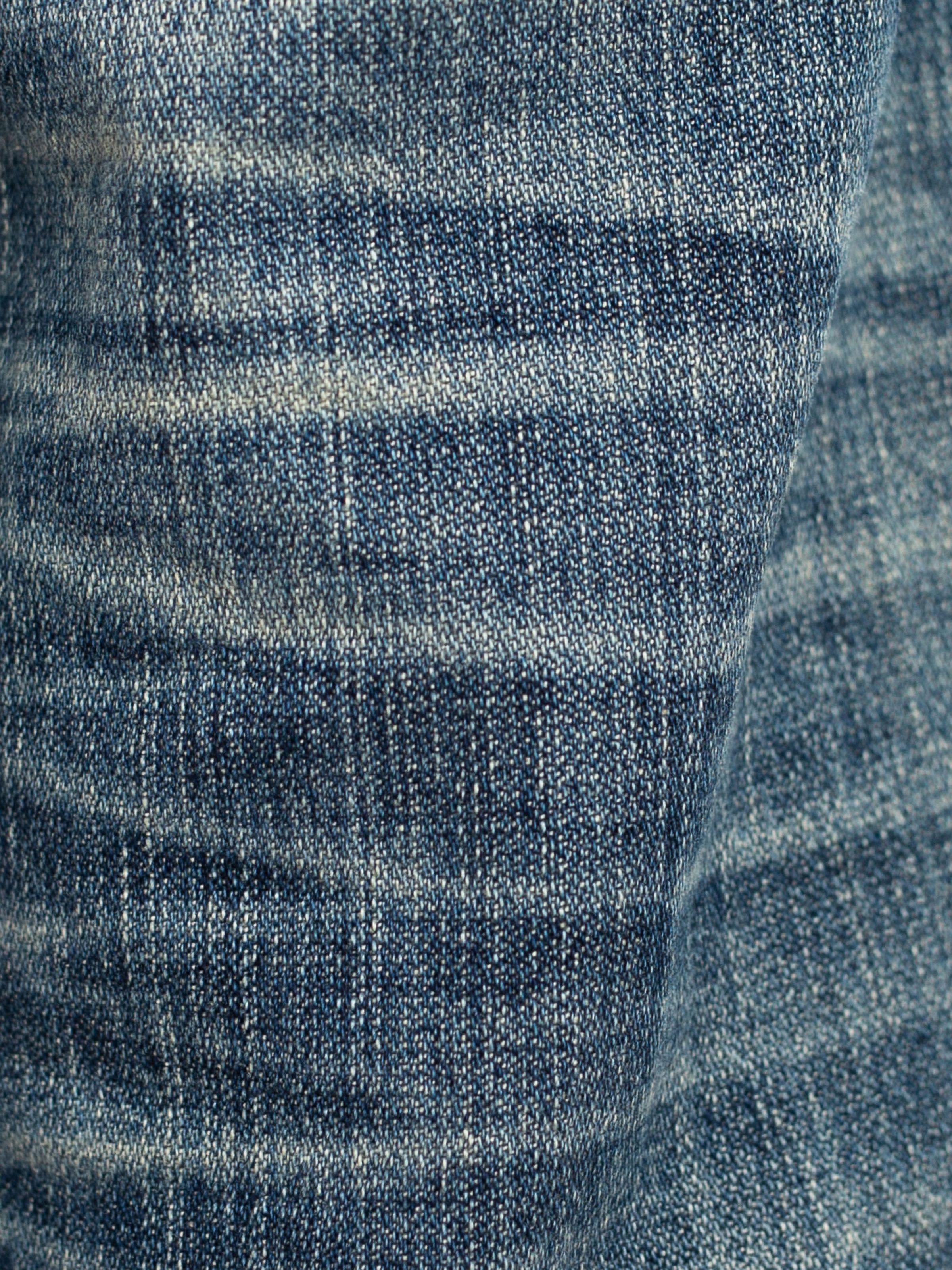 Nudie Jeans Slim Jim Quarter Tracks, close-up of the rigid blue denim with authentic wear marks and vertical streakiness.