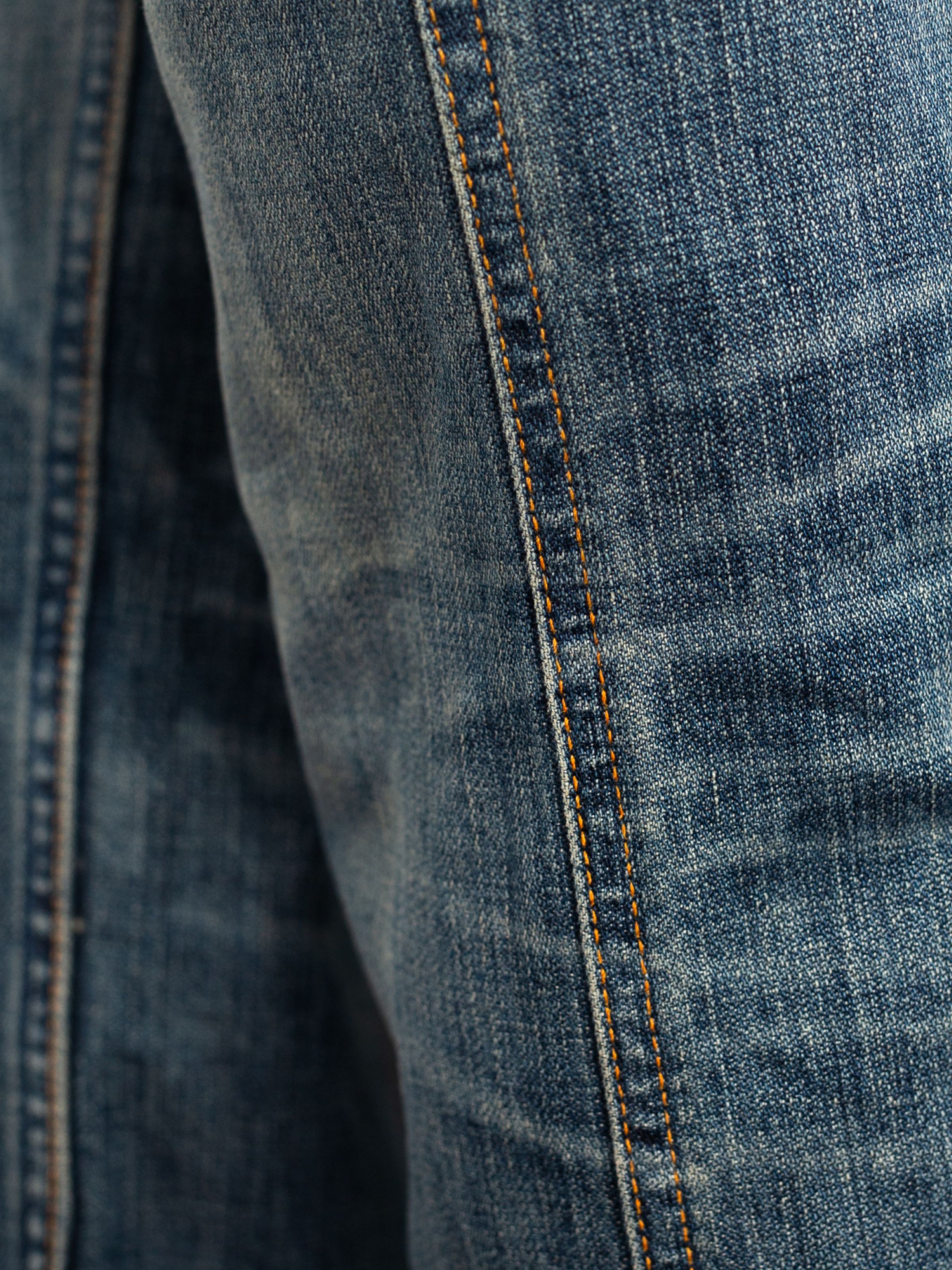 Nudie Jeans Slim Jim Quarter Tracks, close-up of mid blue rigid denim with orange thread at the seams.