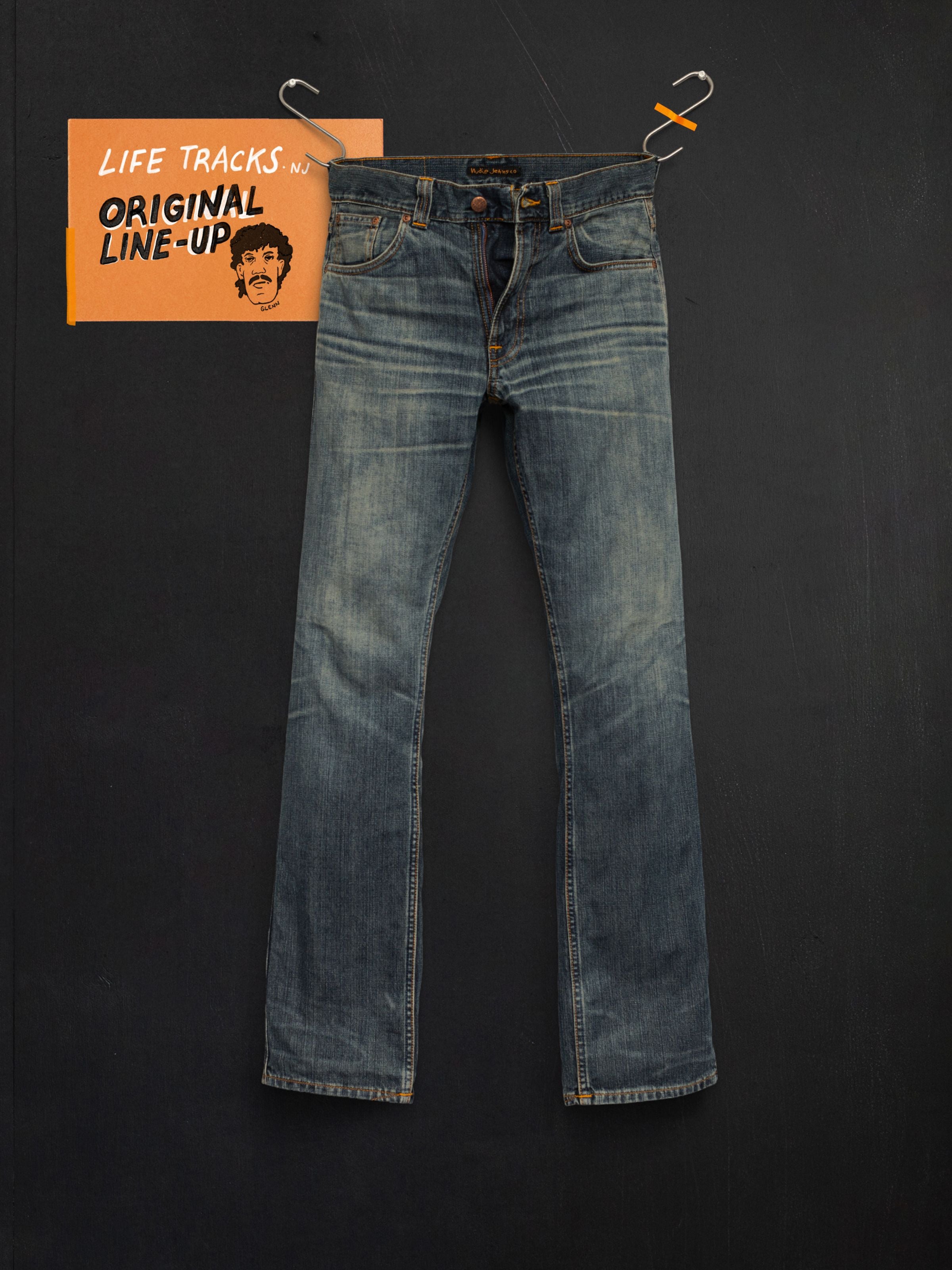 Nudie Jeans Slim Jim Quarter Tracks, Herrenjeans mit schmaler Passform, hängend im Flat-Shot vor dunklem Hintergrund.