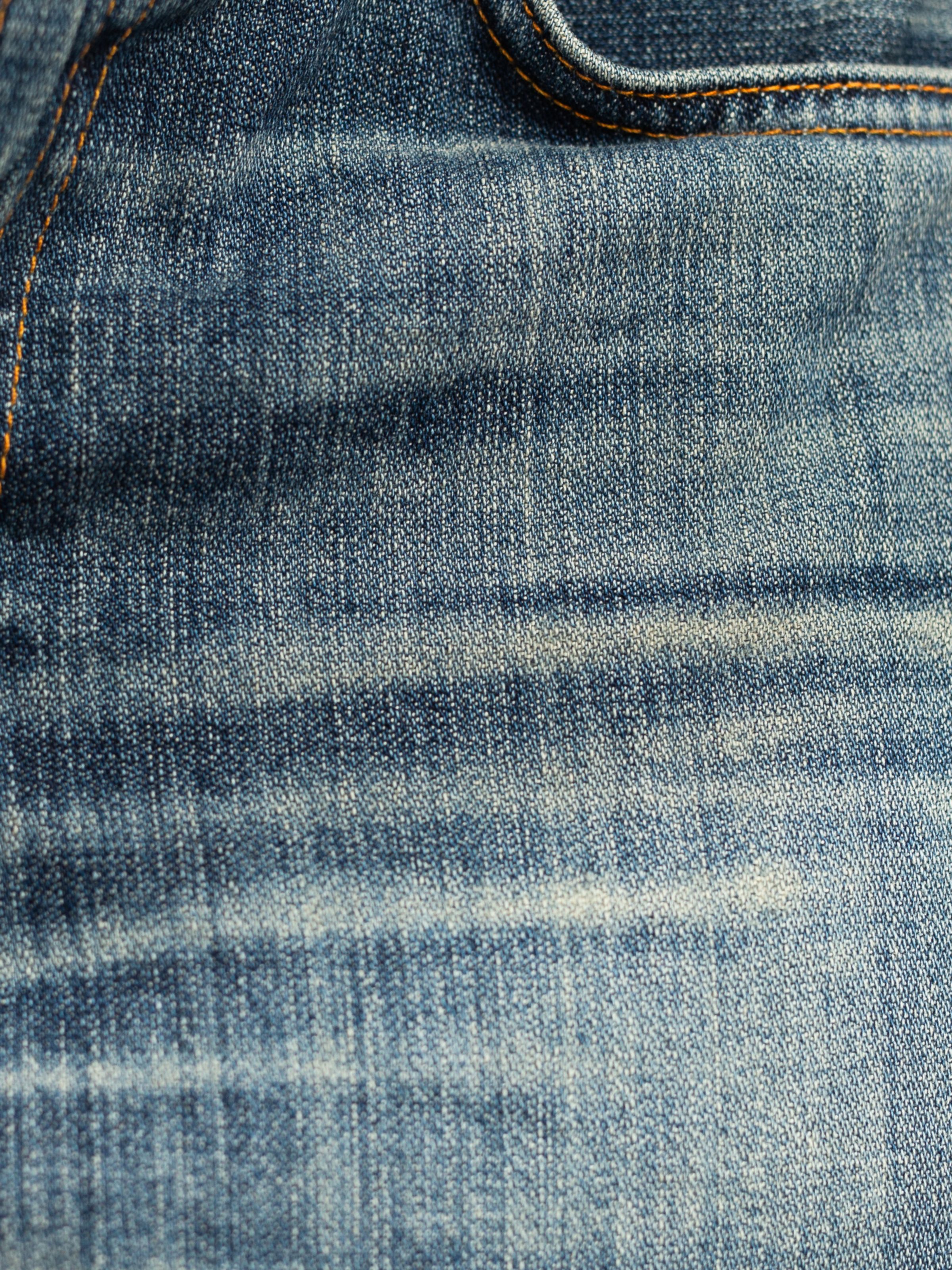 Nudie Jeans Slim Jim Quarter Tracks denim close-up, showing the mid-blue wash with vertical streakiness and wear marks.