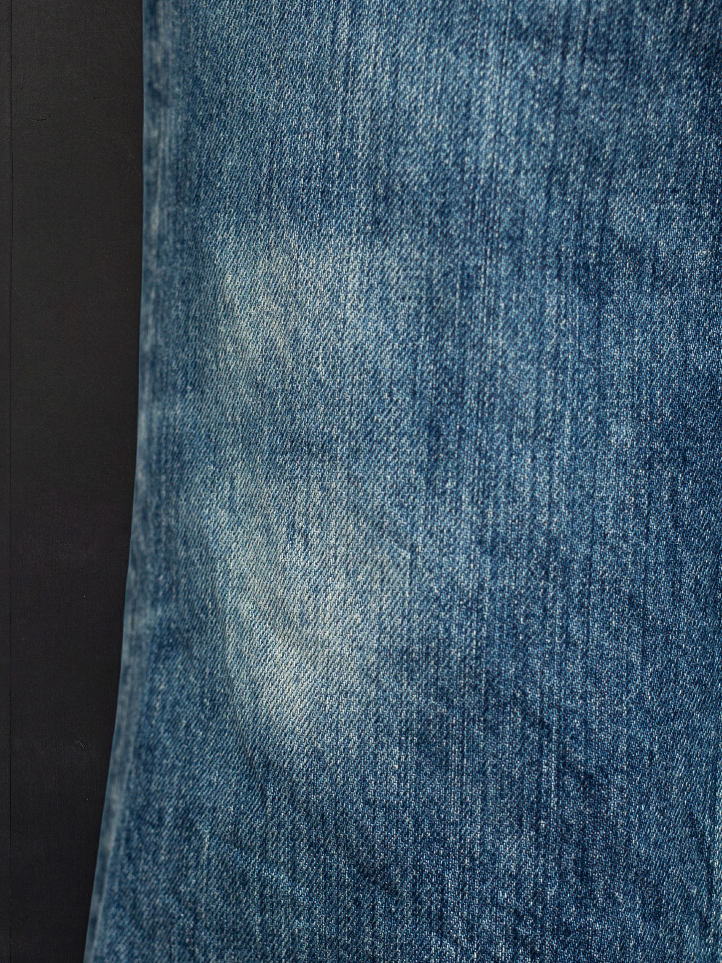 Nudie Jeans Flare Glenn Lineage Tracks, close-up of rigid organic denim with deep indigo tones and authentic streakiness.