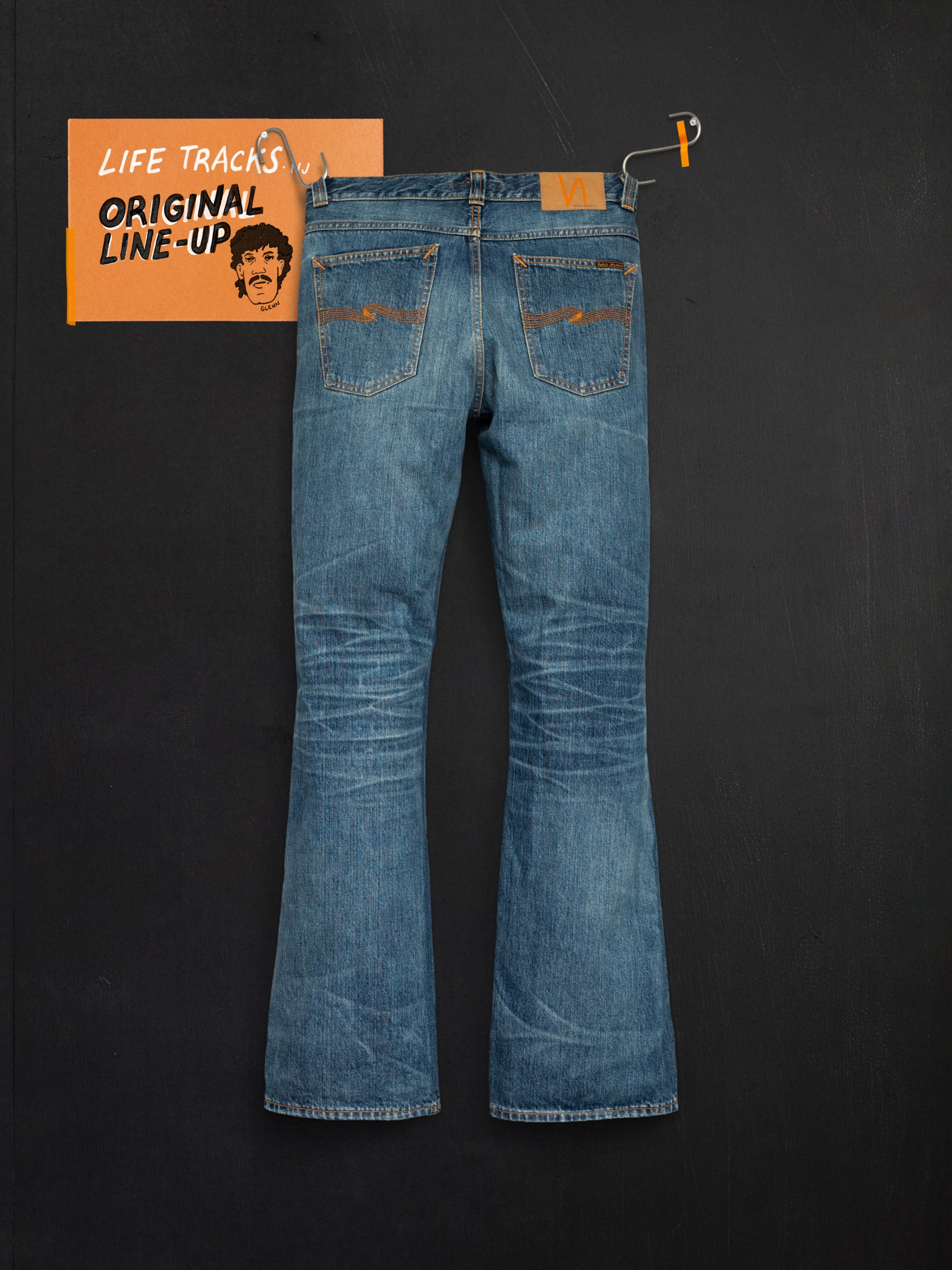 Nudie Jeans Flare Glenn Lineage Tracks, mid blue flared jeans from the back with orange stitching and worn-in fades.