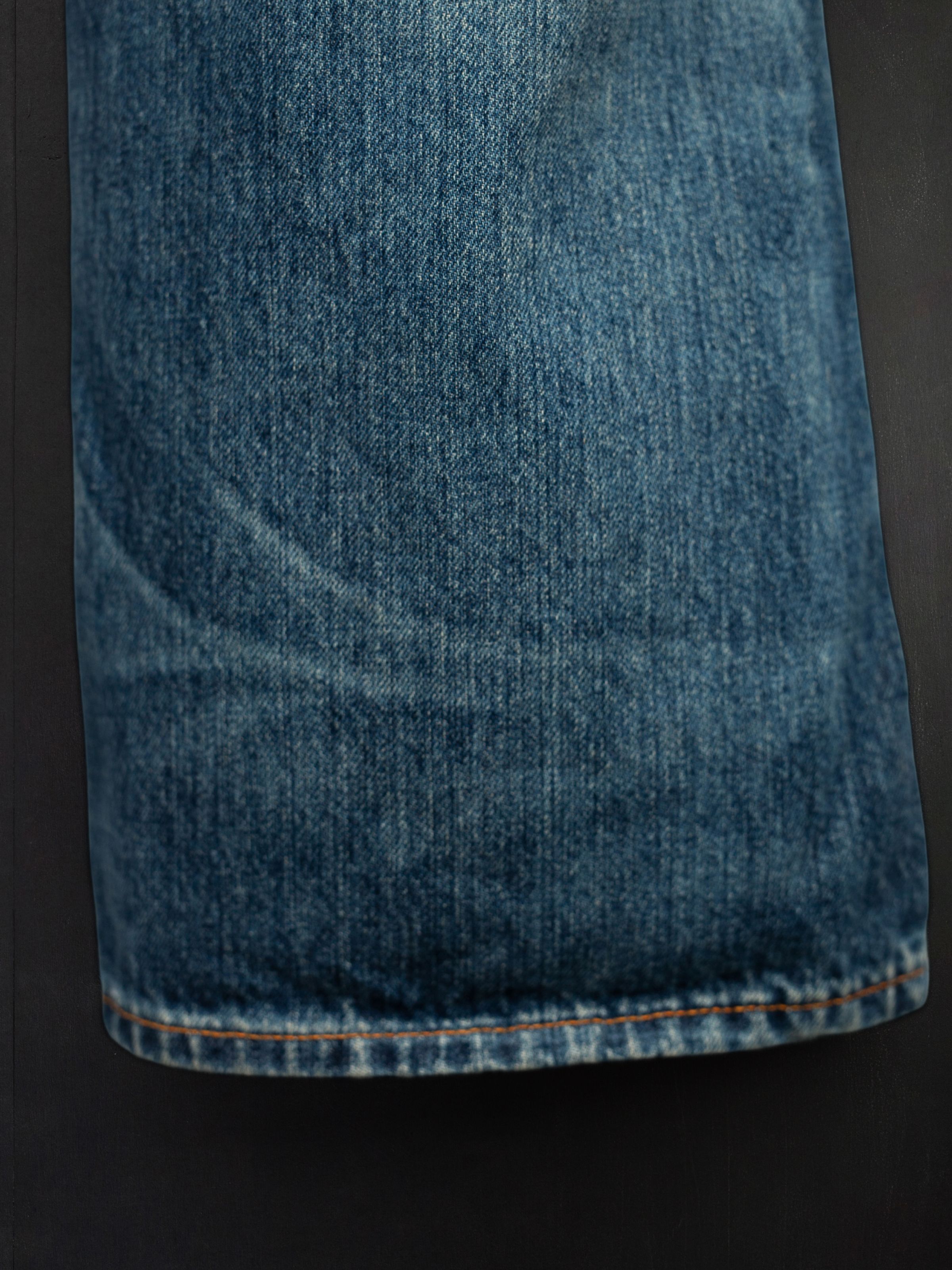 Nudie Jeans Flare Glenn Lineage Tracks, close-up of the flared leg hem in mid blue washed rigid denim with orange thread.