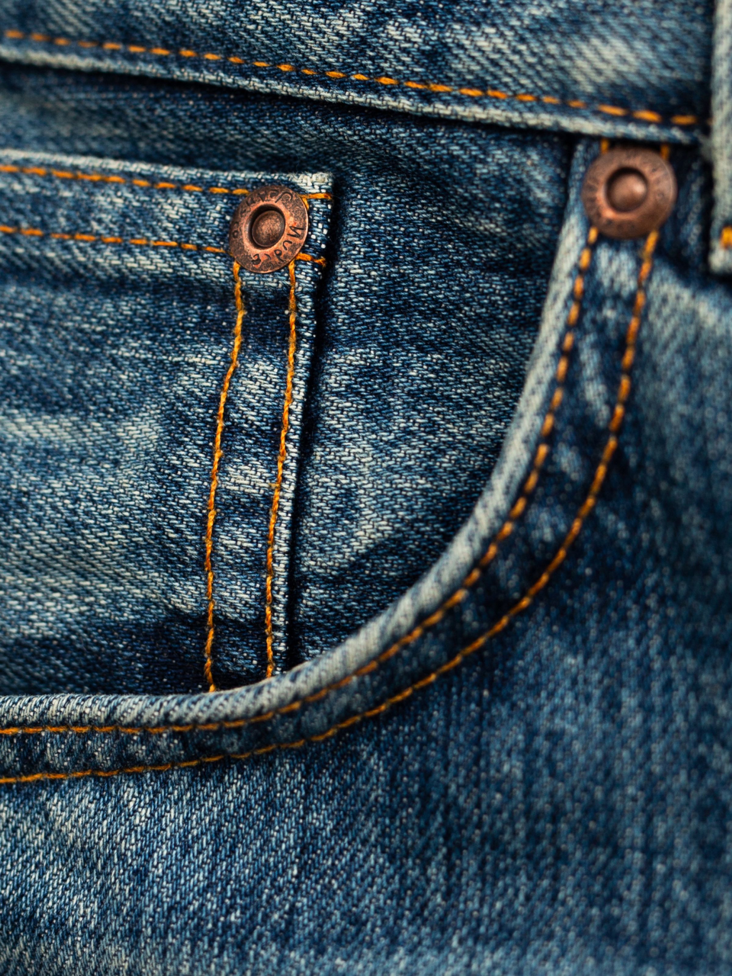 Nudie Jeans Flare Glenn Lineage Tracks, close-up of the front pocket with copper rivets and orange stitching.