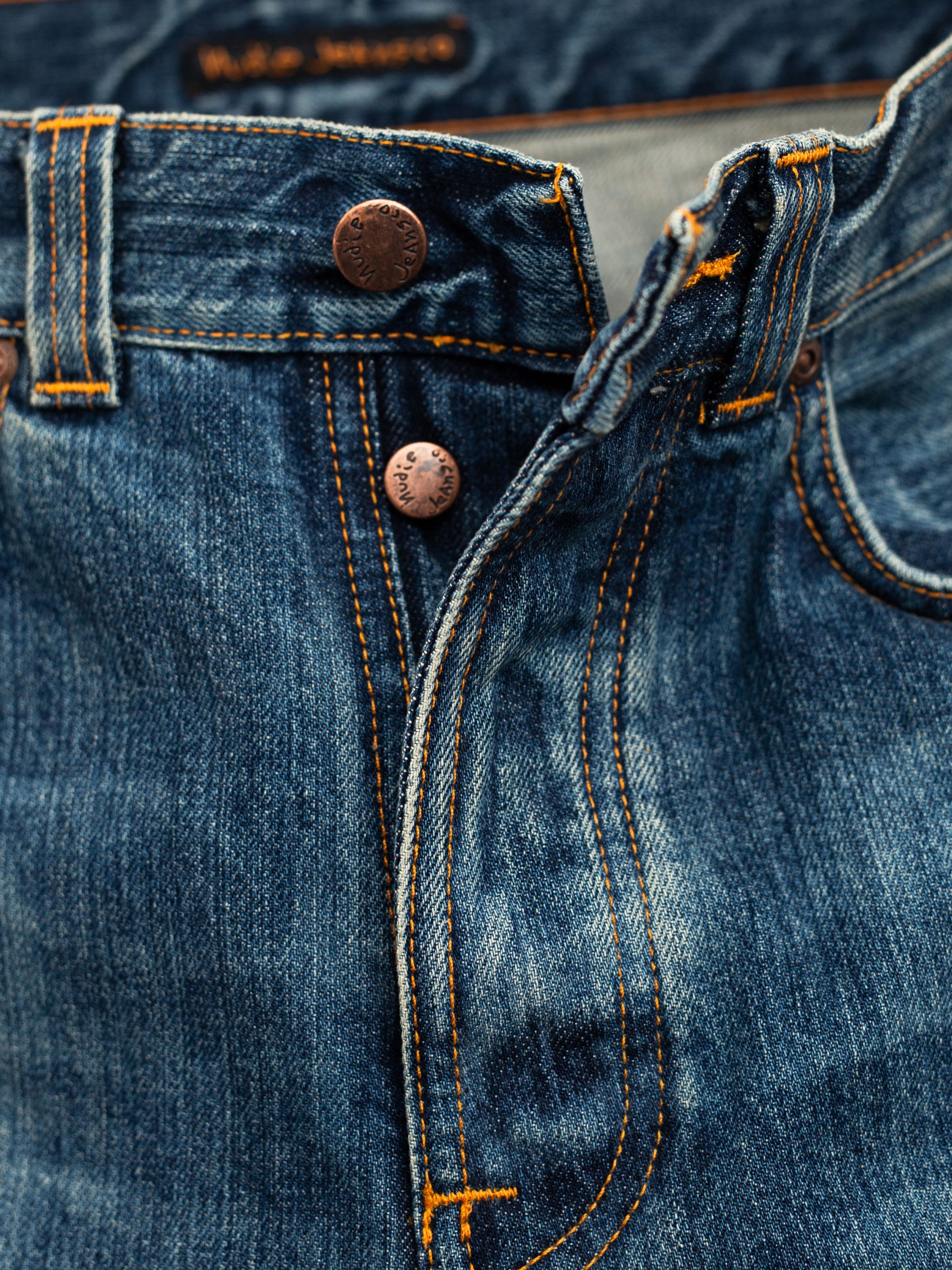 Nudie Jeans Flare Glenn Lineage Tracks, a close-up of the copper button fly and orange stitching on mid blue rigid denim.