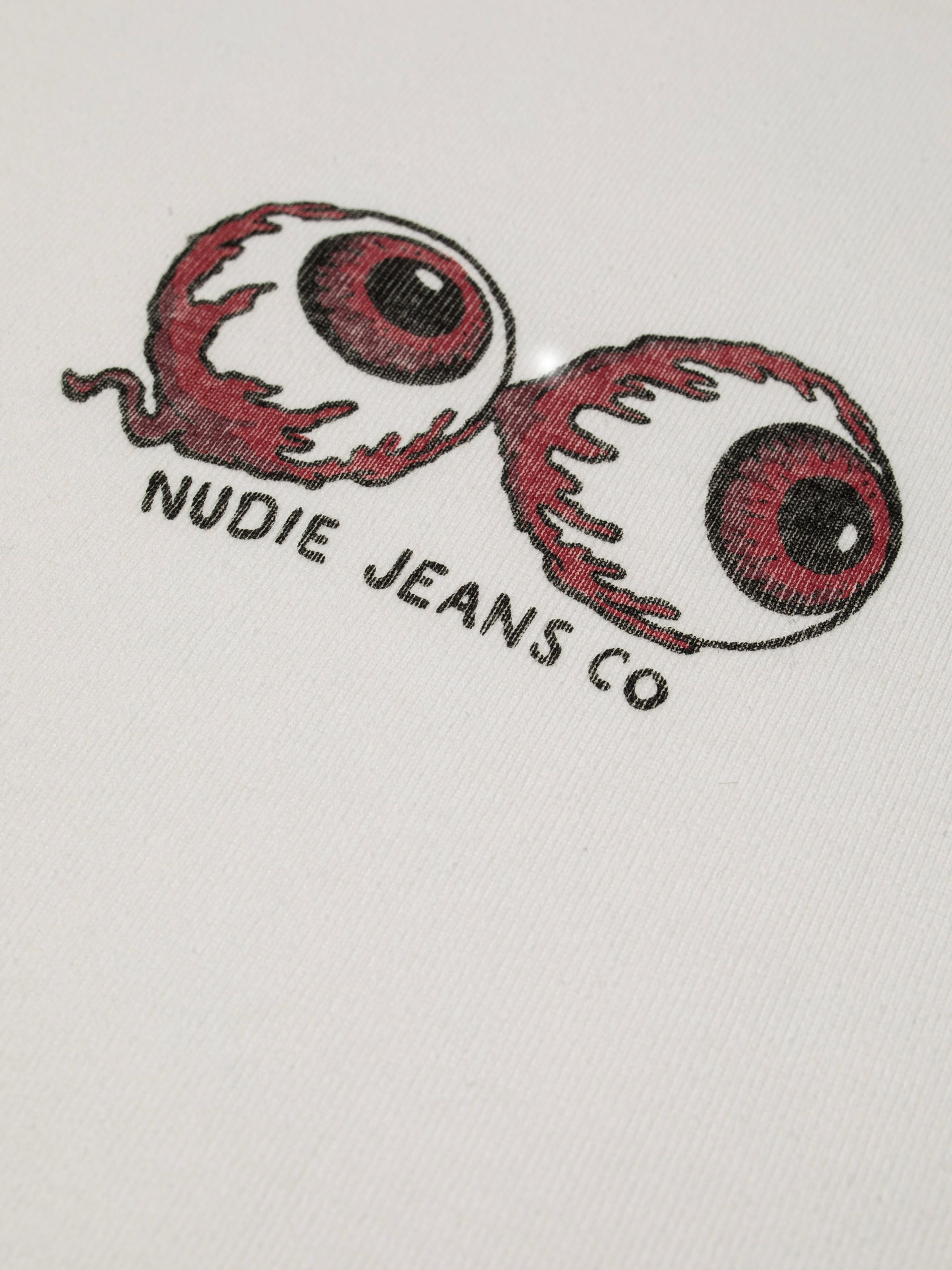 Nudie Jeans Eve T-Shirt Eyeballs in Offwhite, close-up of the red eyeball graphic and logo on organic cotton rib knit.