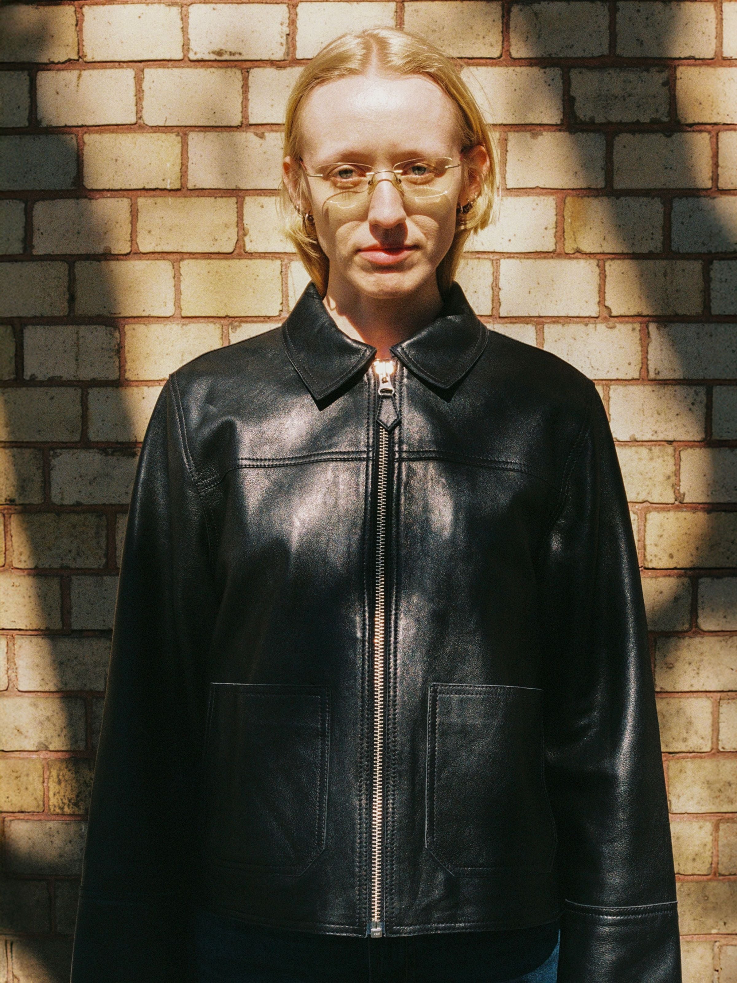Nudie Jeans Anja Zip Jacket Leather in Black, a supple lamb skin leather jacket shown on a model against a brick wall.