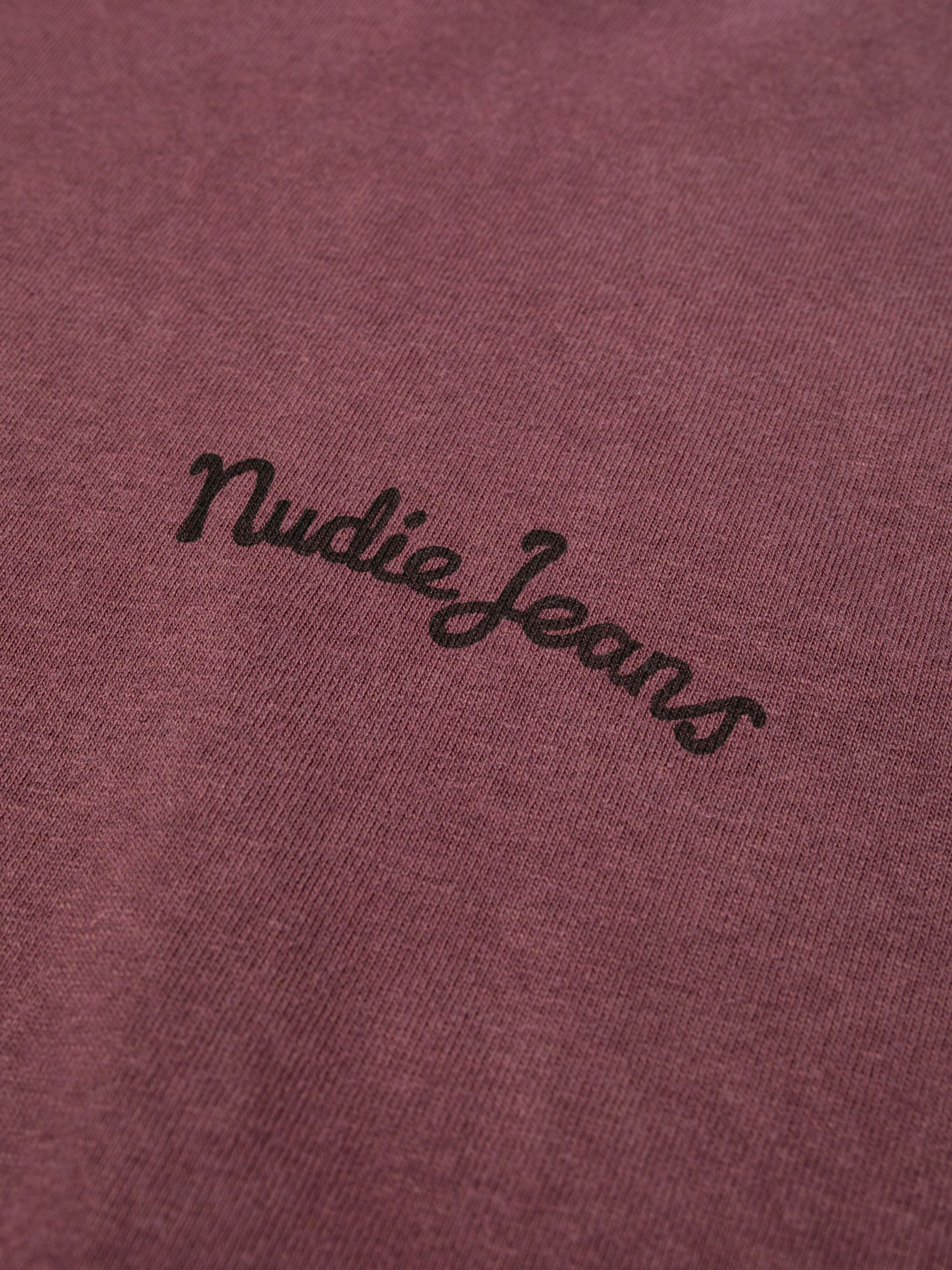 Nudie Jeans Karita T-Shirt in Burgundy, close-up of the black script logo print on organic cotton.