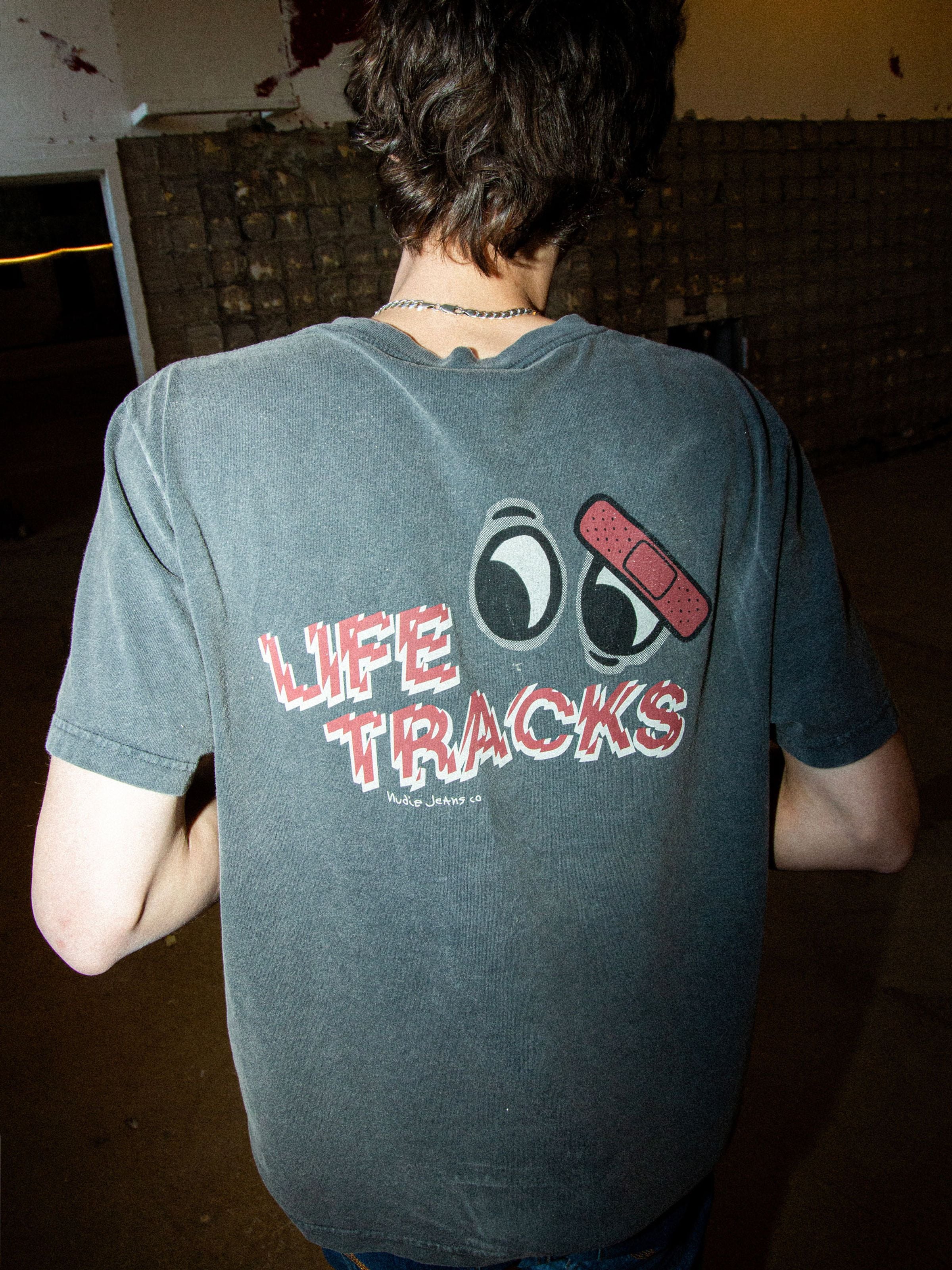 Nudie Jeans Roy T-Shirt Life Tracks I in Antracite, an organic cotton t-shirt with back graphic print on a model.