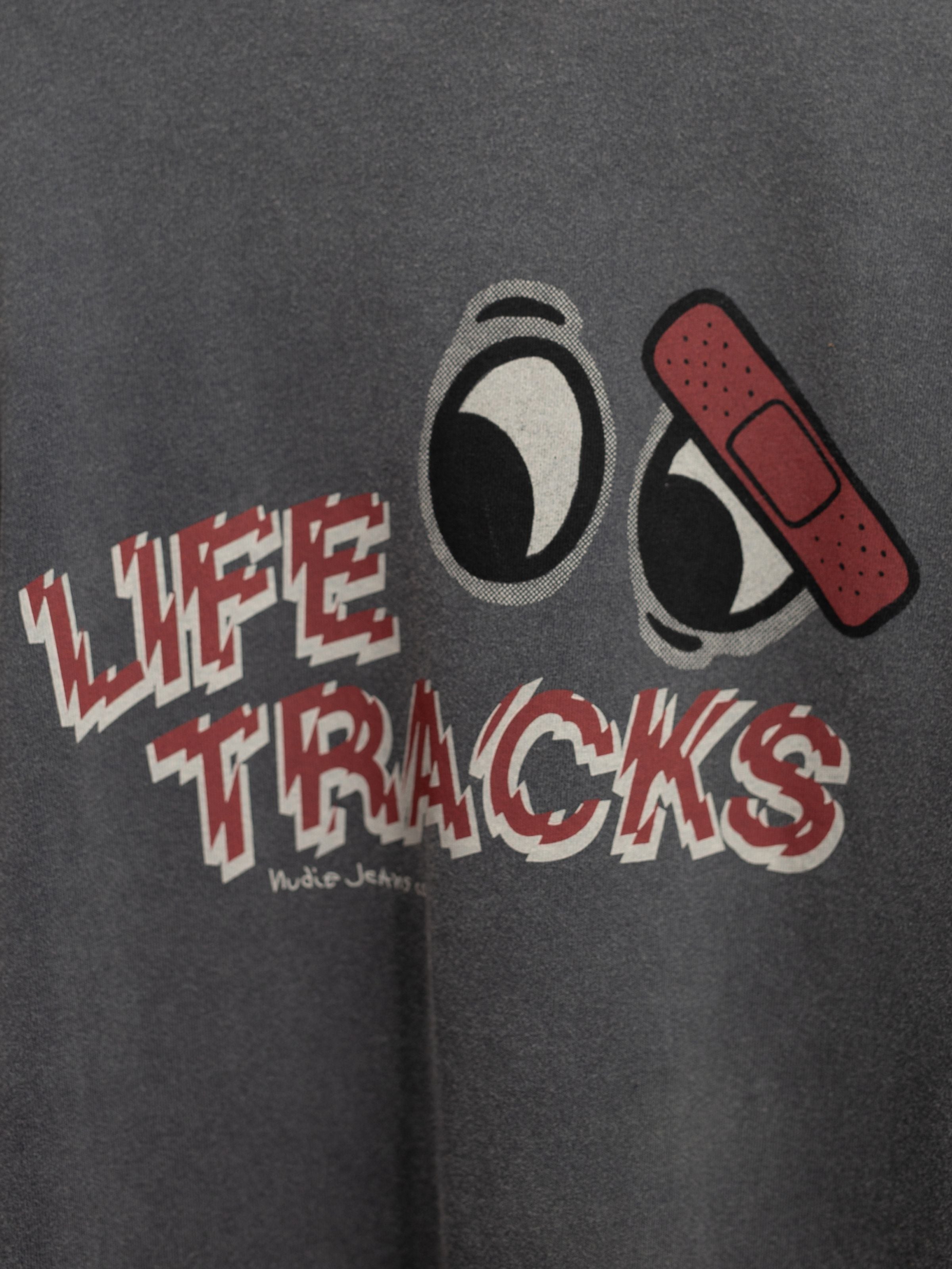 Nudie Jeans Roy T-Shirt Life Tracks I Antracite, a close-up of the graphic print on faded organic cotton fabric.