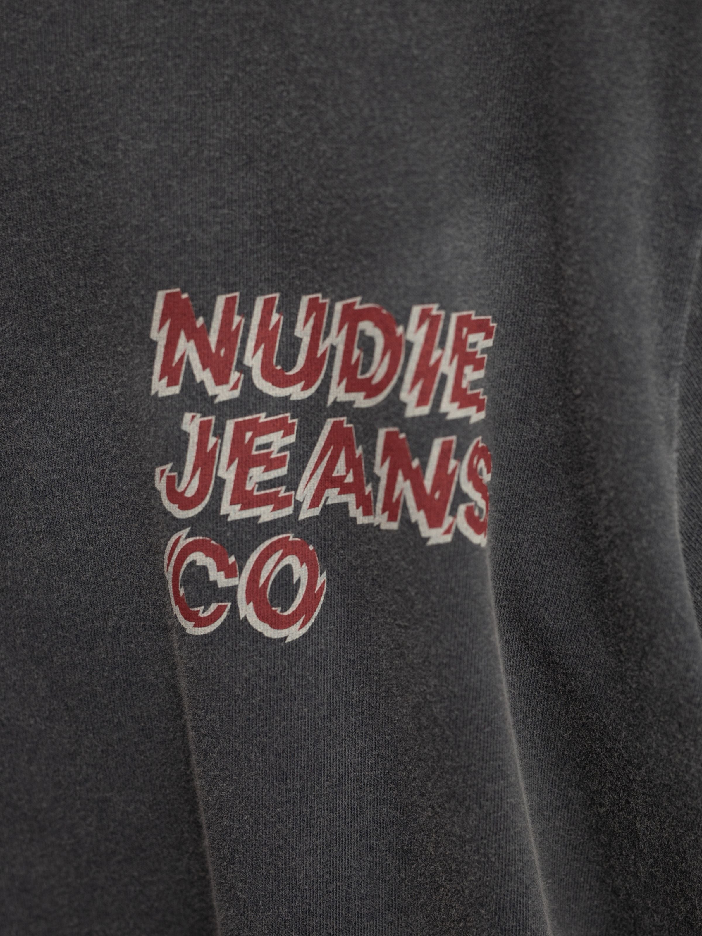 Nudie Jeans Roy T-Shirt Life Tracks I Antracite, a close-up of the red and white graphic logo on organic cotton jersey.