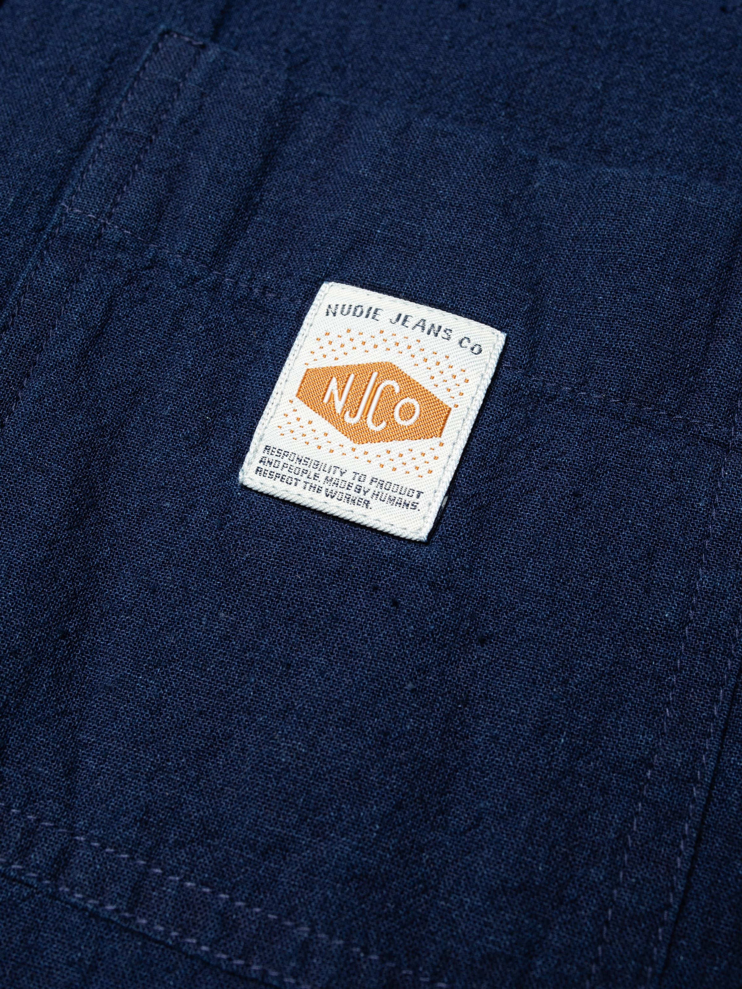 Nudie Jeans Nila Shirt Dress in Indigo Blue, close-up of the woven logo label on the indigo-dyed organic cotton and linen.