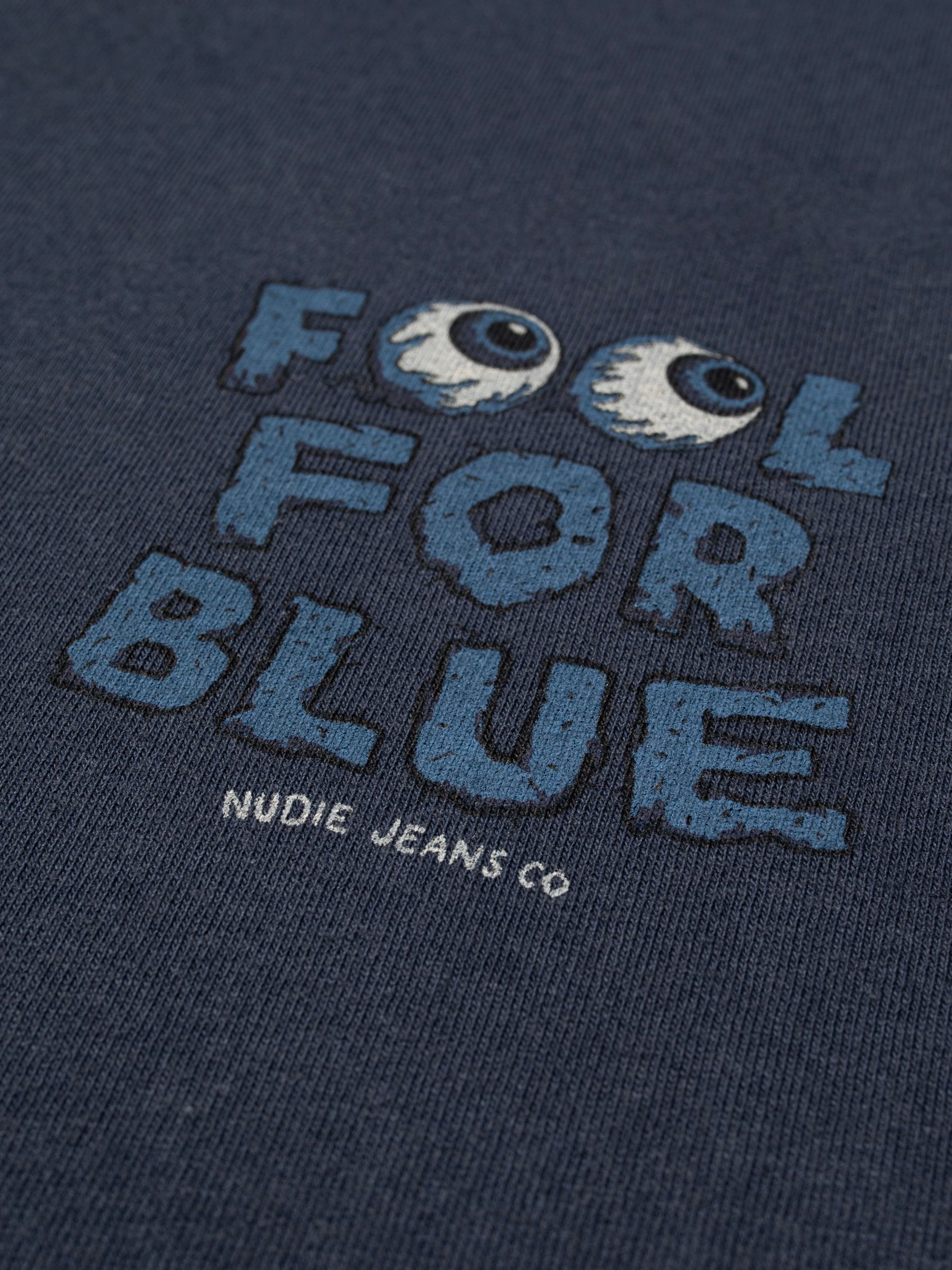 Nudie Jeans Roy T-Shirt Freaky Dark Blue, eine Nahaufnahme der FOOL FOR BLUE Augapfel-Grafik auf Bio-Baumwolle.
